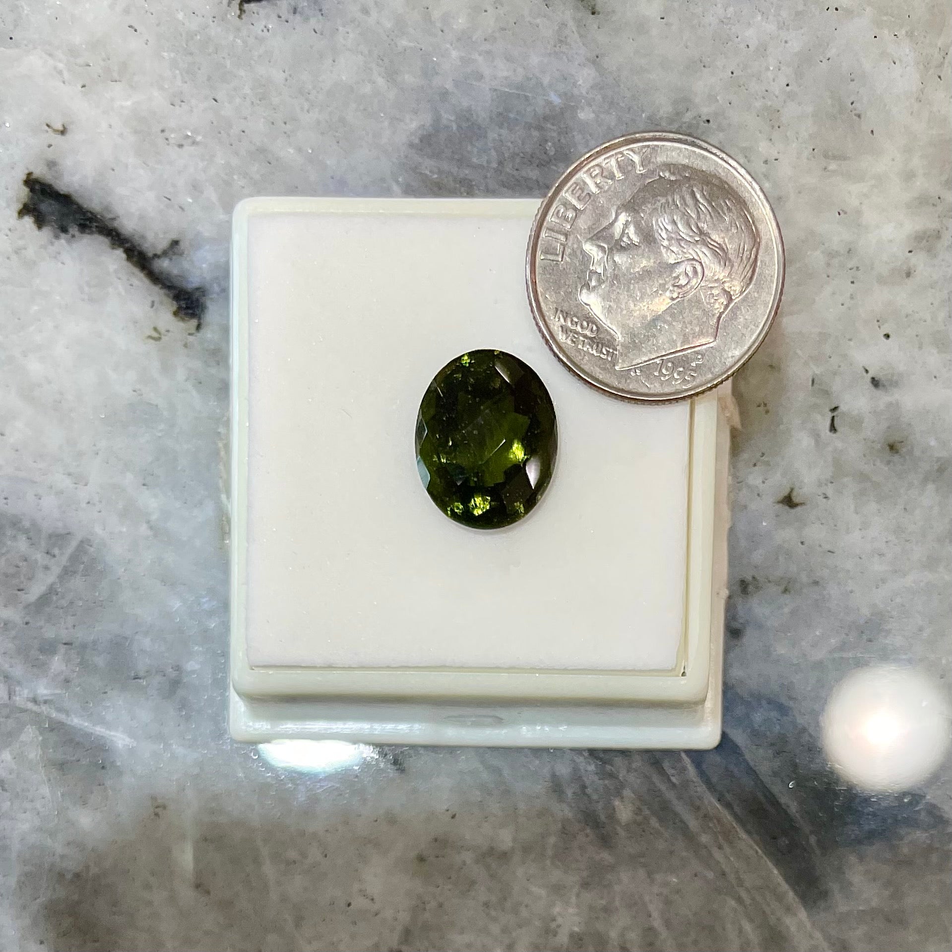 A faceted oval checkerboard cut moldavite gemstone that weighs 4.14 carats.