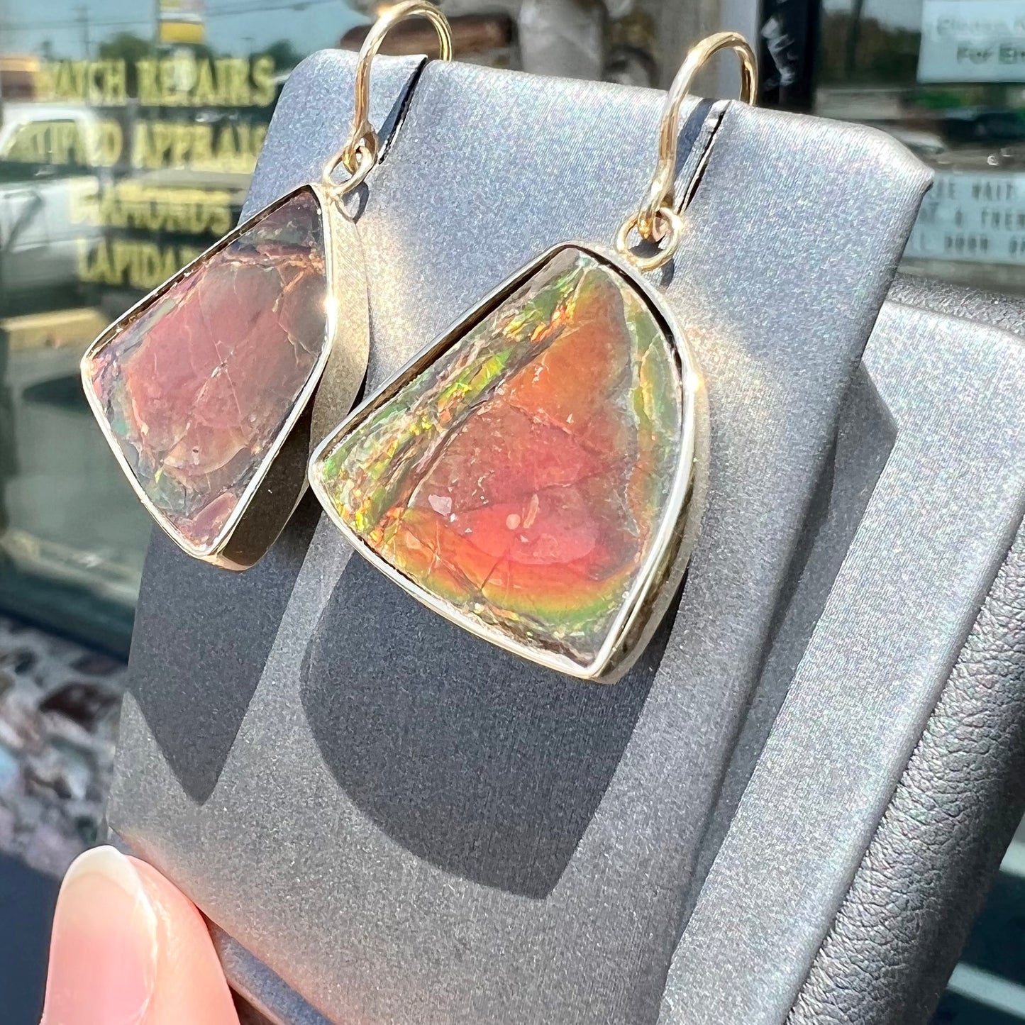 Yellow gold French wire dangle earrings bezel set with two polished freeform cut red ammolite fossils.