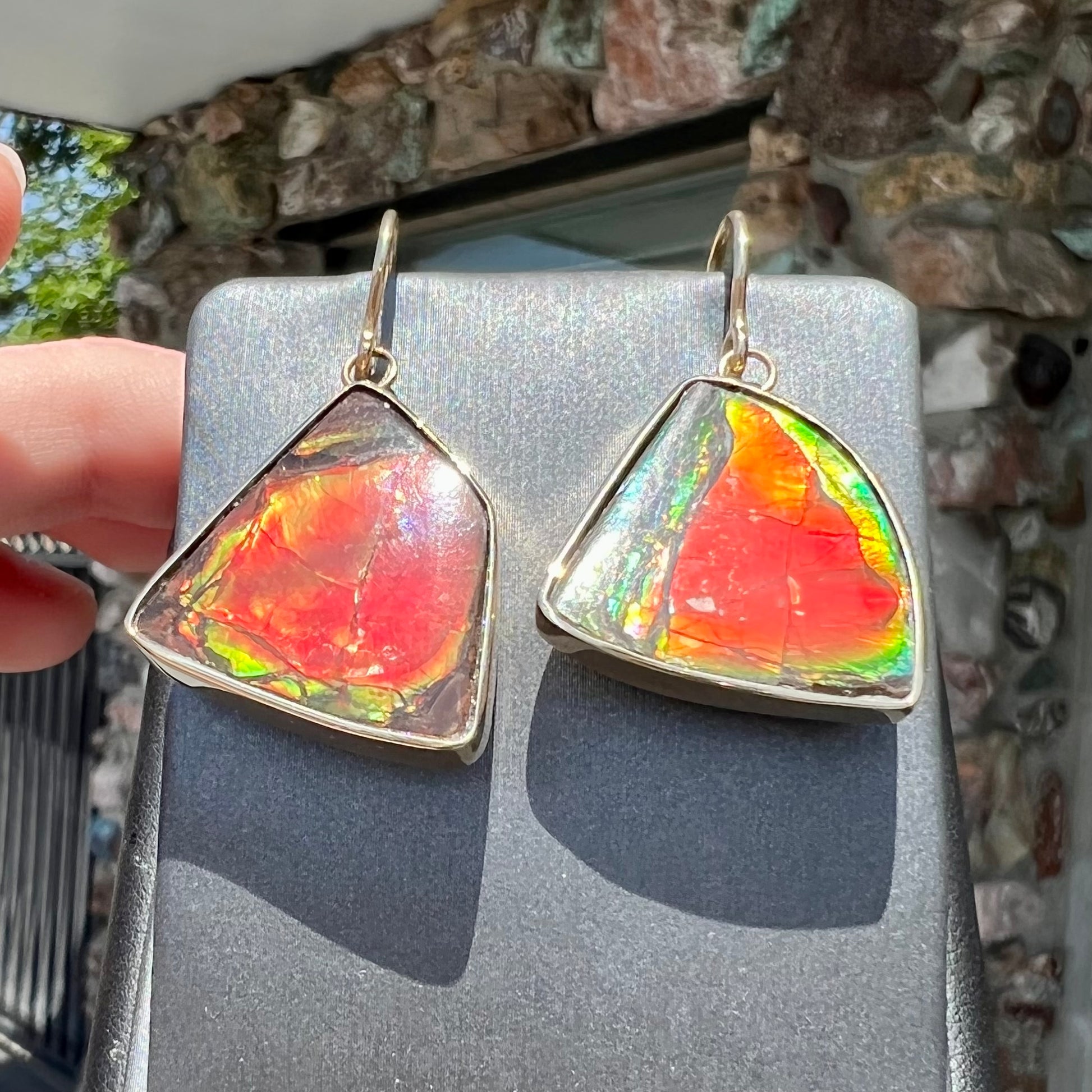 Yellow gold French wire dangle earrings bezel set with two polished freeform cut red ammolite fossils.