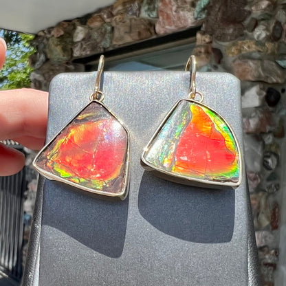 Yellow gold French wire dangle earrings bezel set with two polished freeform cut red ammolite fossils.