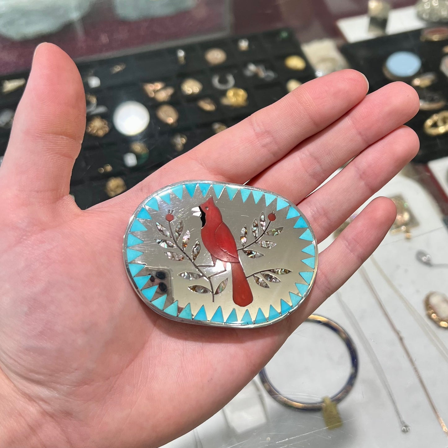 A Zuni belt buckle featuring a red cardinal inlaid with coral, handmade by artists Dennis and Nancy Edaakie.