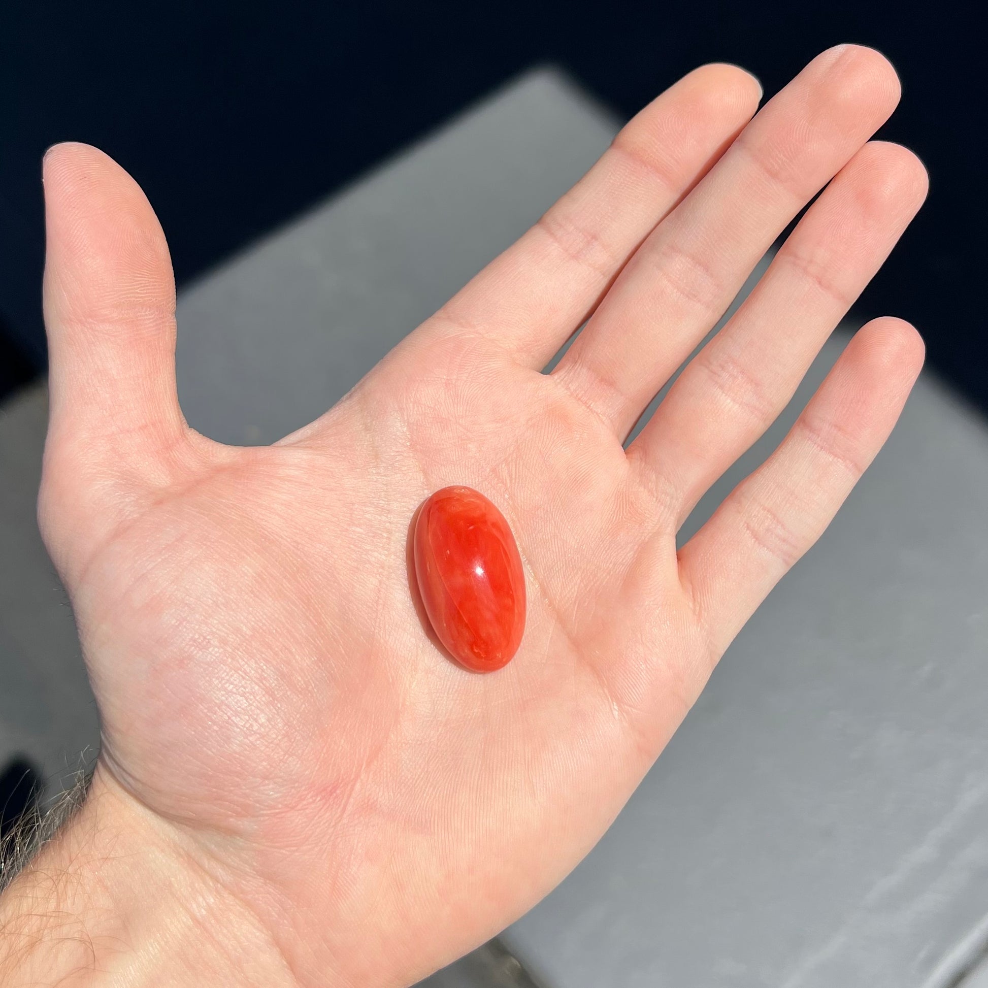 A large, loose red-orange coral cabochon that measures 1.2 inches by 0.7 inches.