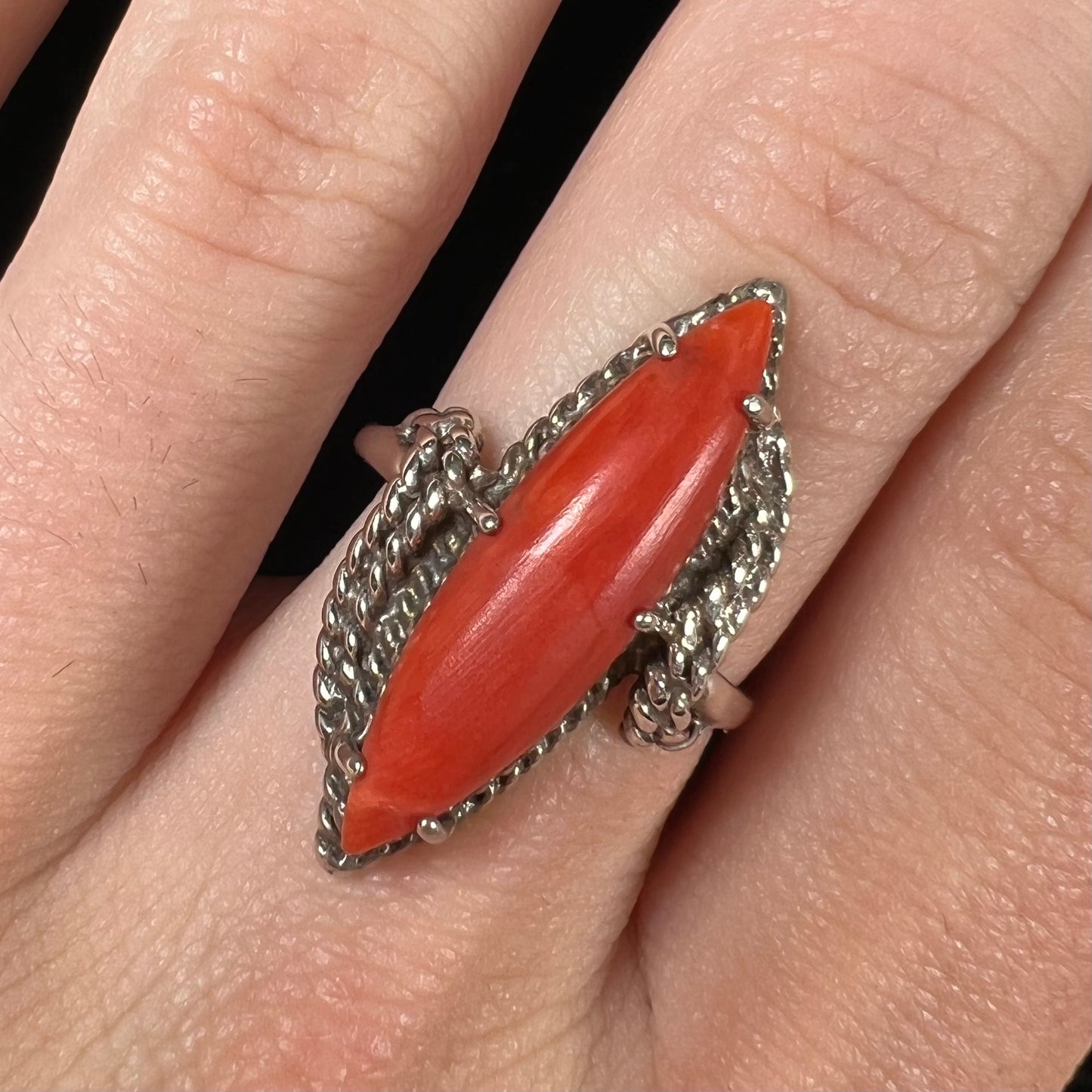 A prong-set silver ring set with a red marquise cut coral.