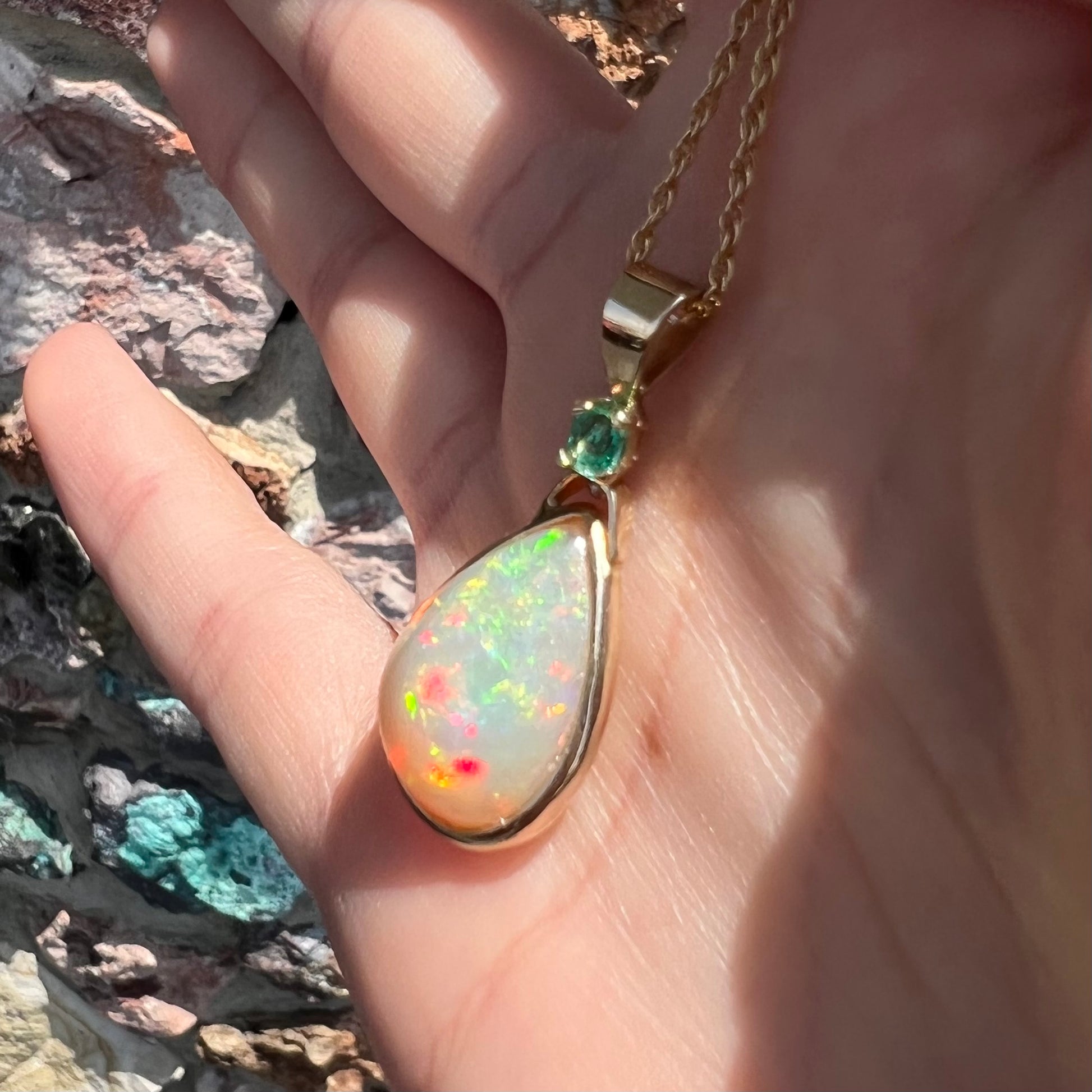 A yellow gold bezel set Ethiopian fire opal drop pendant.  There is an emerald set in the bail.