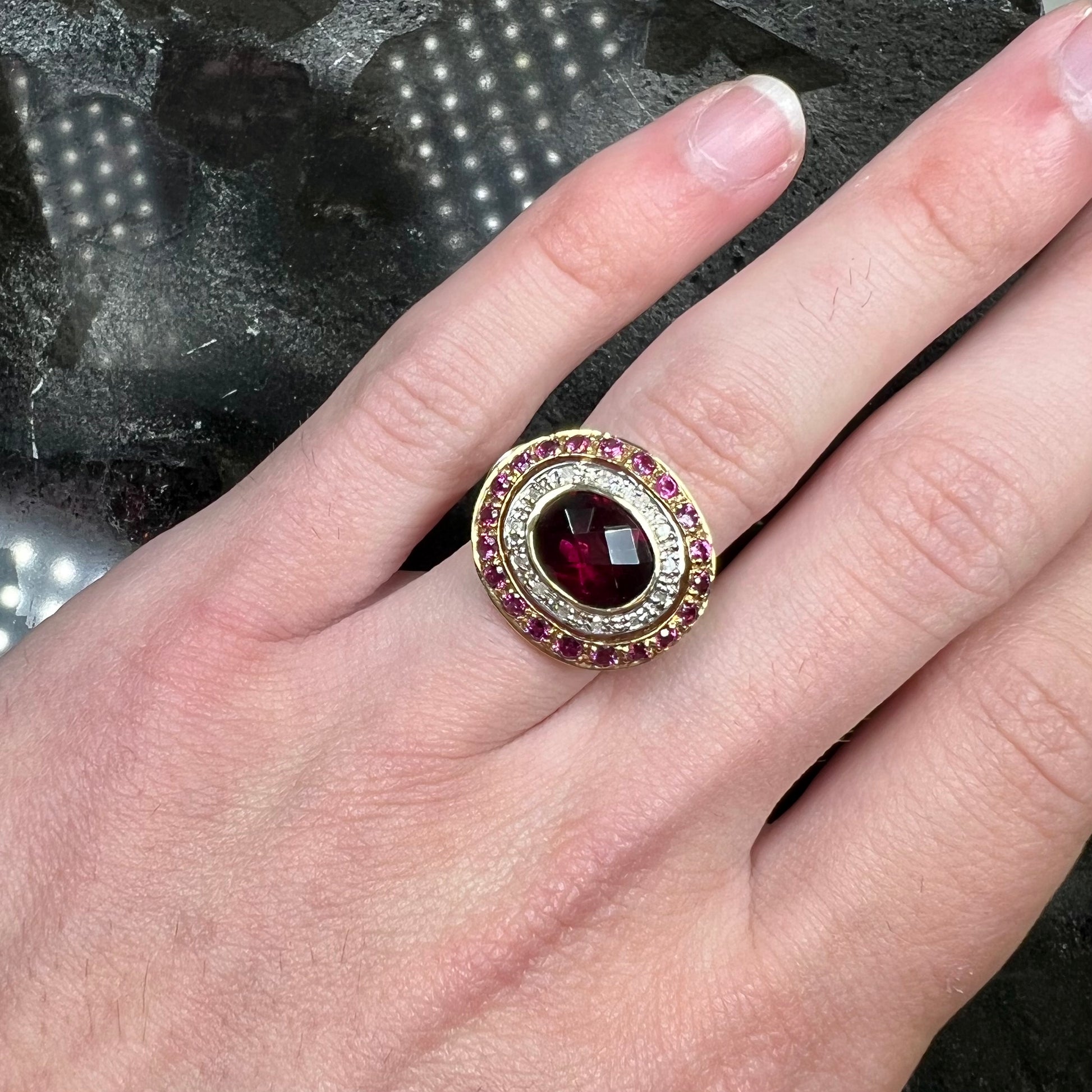 A yellow gold garnet and diamond halo ring set with a checkerboard cut rhodolite garnet center stone.