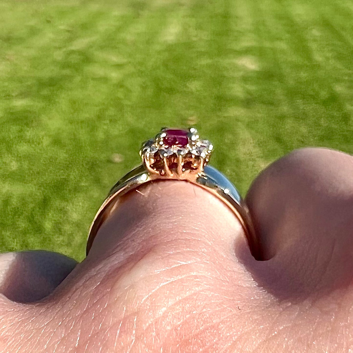 A yellow gold ring set with an emerald cut red ruby surrounded by a halo of round diamonds.