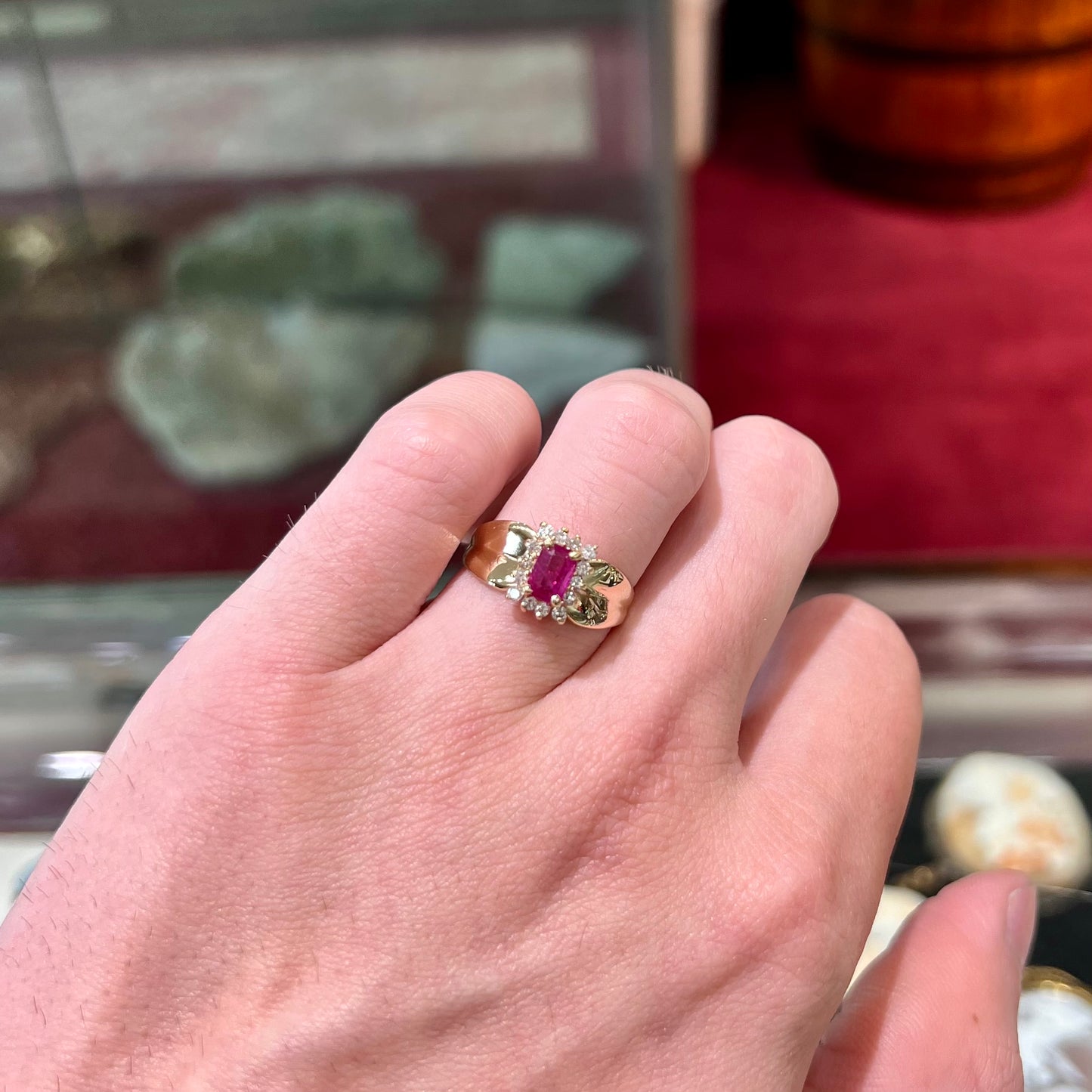 A yellow gold ring set with an emerald cut red ruby surrounded by a halo of round diamonds.