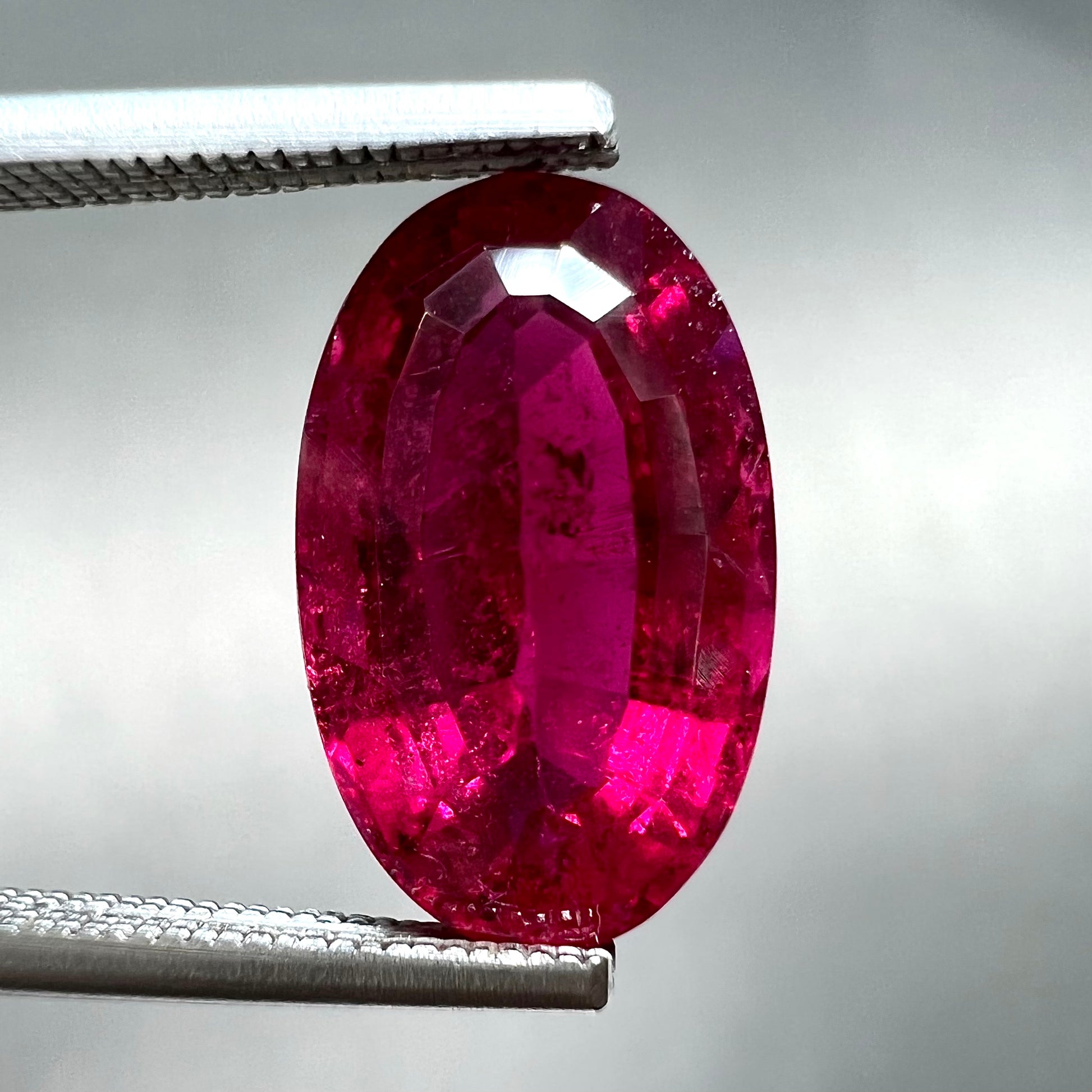 A loose, oval cut, purplish red rubellite tourmaline stone.