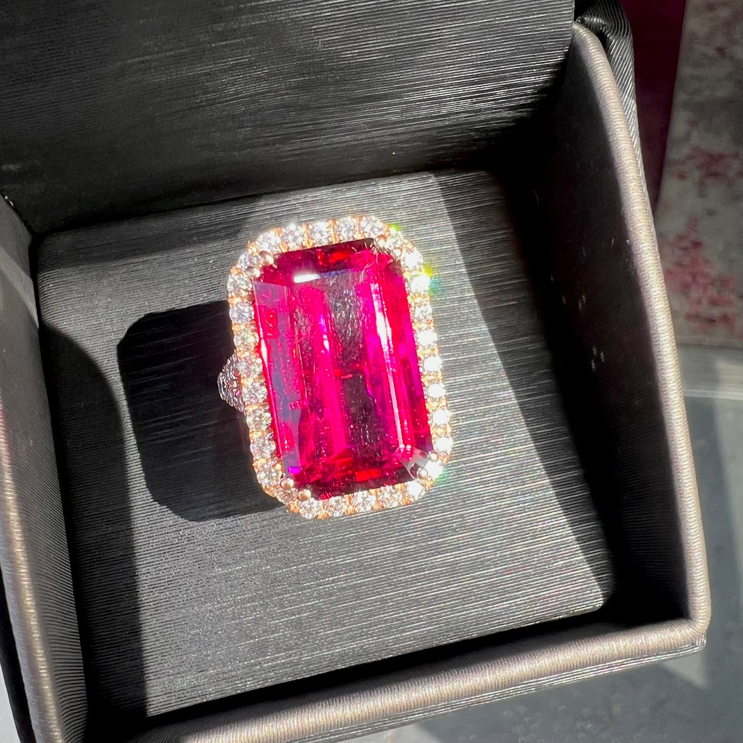 Red emerald cut rubellite tourmaline gemstone set with near flawless round cut diamonds in rose gold.