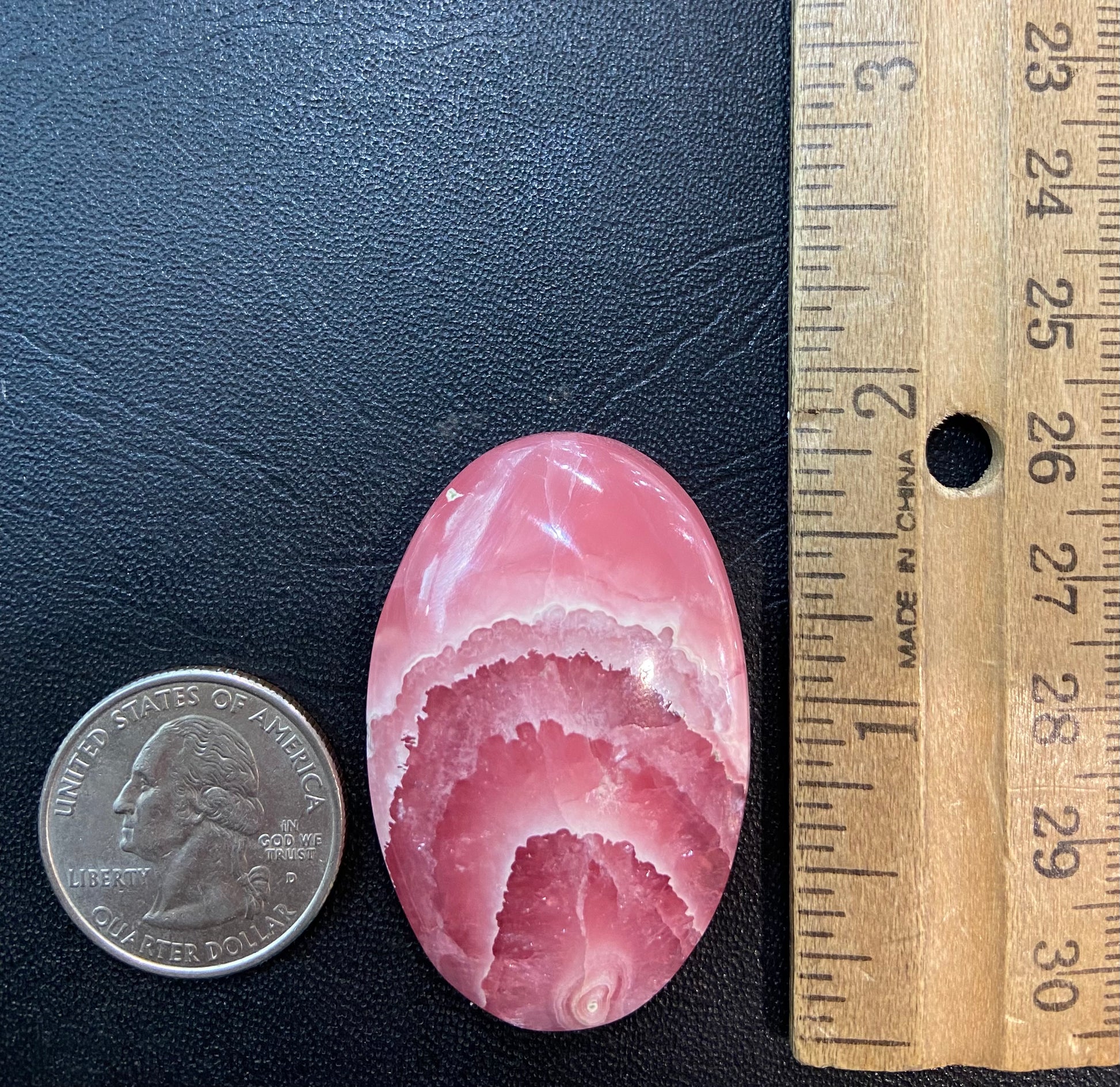 An oval cabochon cut pink rhodochrosite stone.