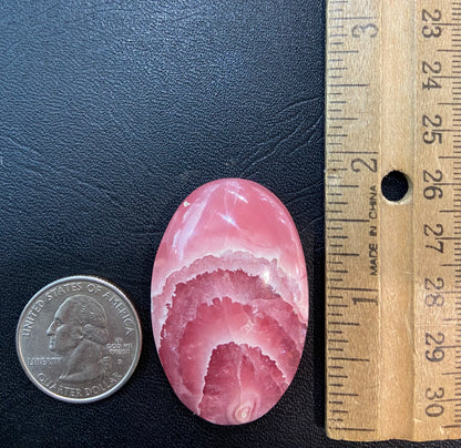 An oval cabochon cut pink rhodochrosite stone.