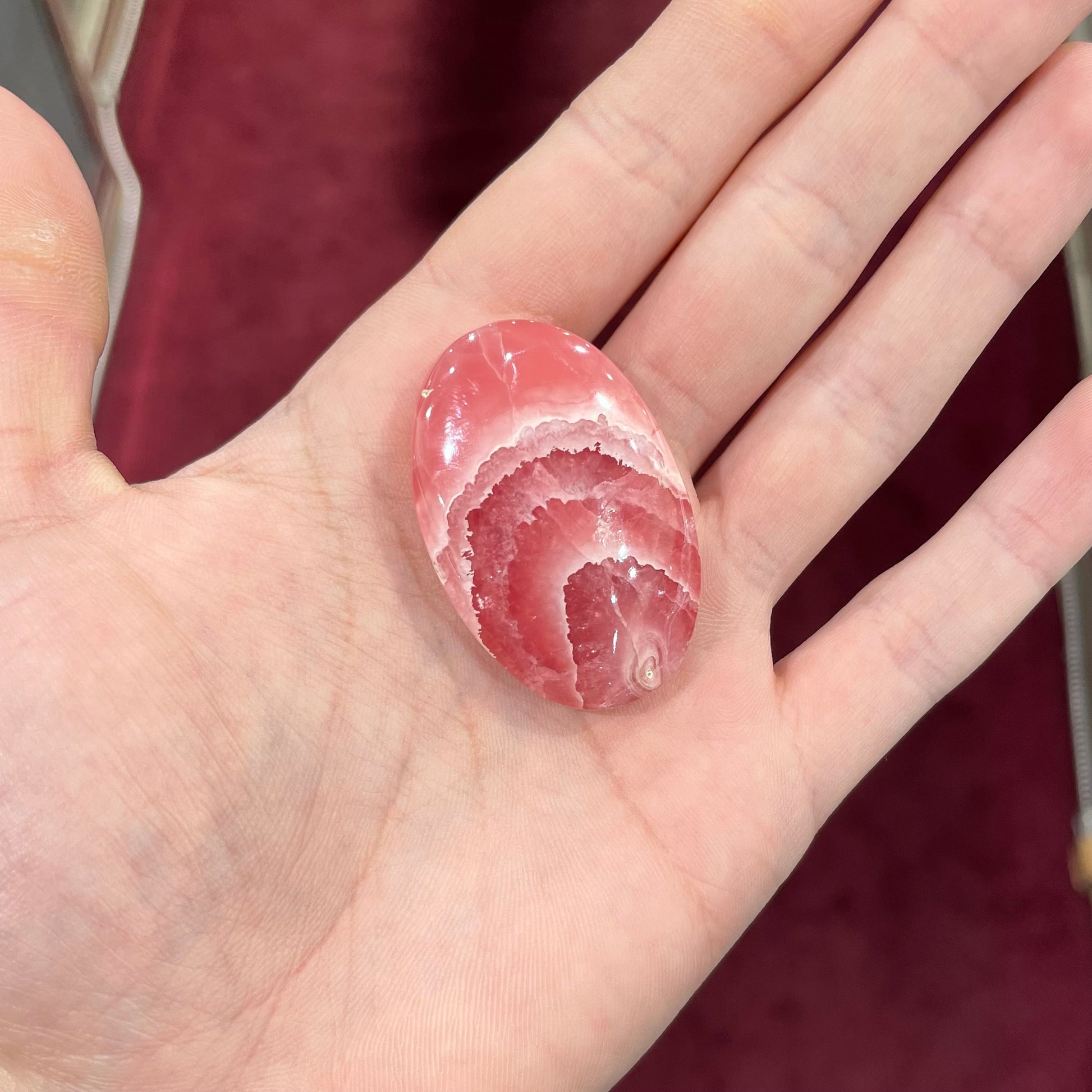 An oval cabochon cut pink rhodochrosite stone.