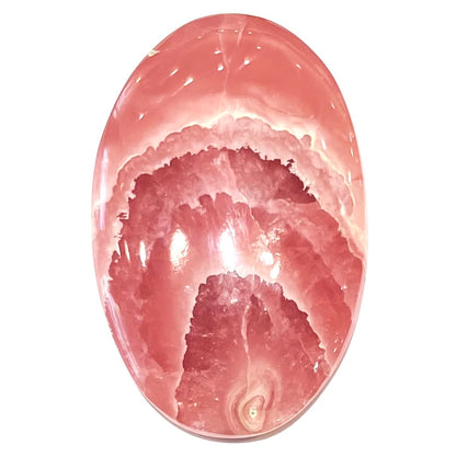 An oval cabochon cut pink rhodochrosite stone.