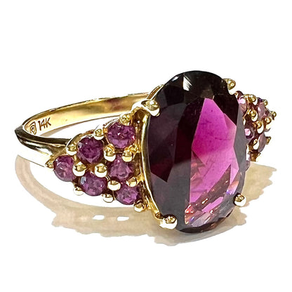 A yellow gold ring stamped "14K" set with clusters of purple garnets set on each side of a rhodolite garnet.