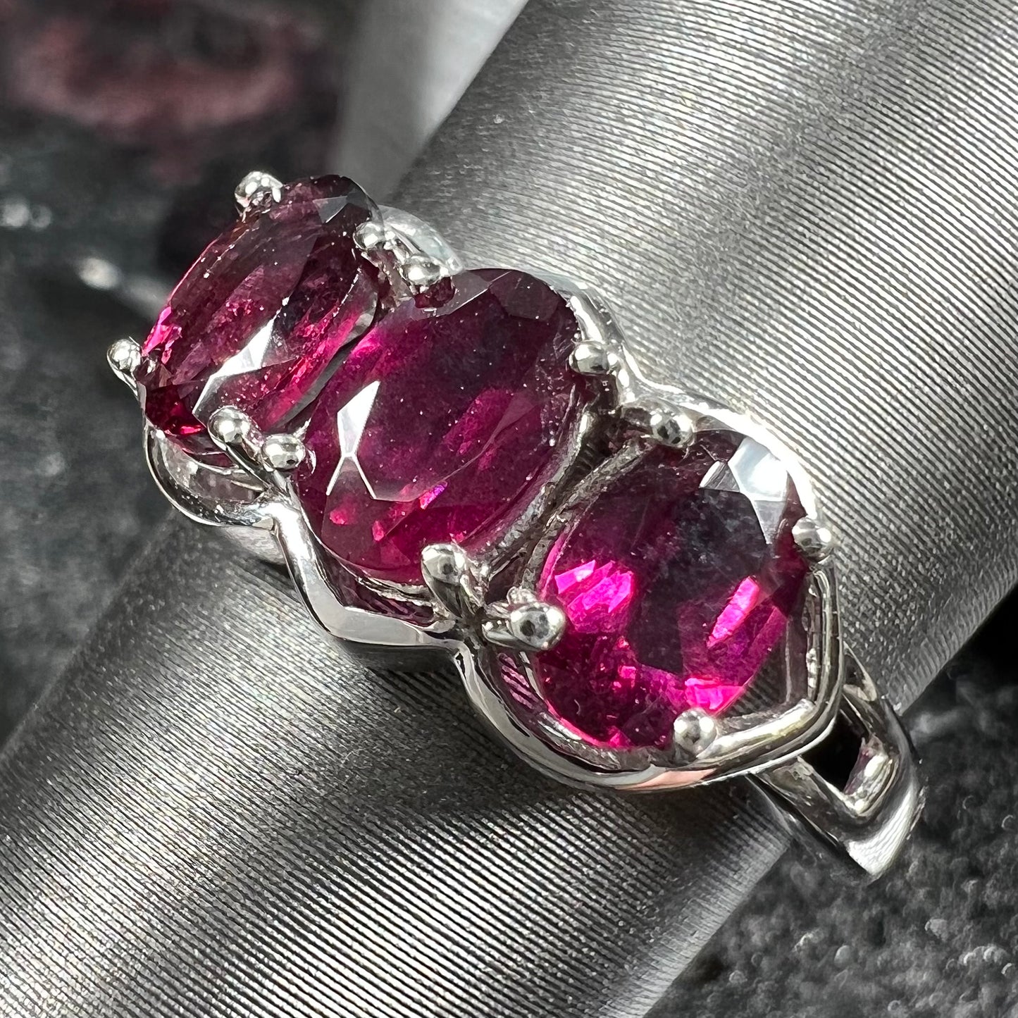 A three stone past, present, and future purple faceted oval cut rhodolite garnet ring.