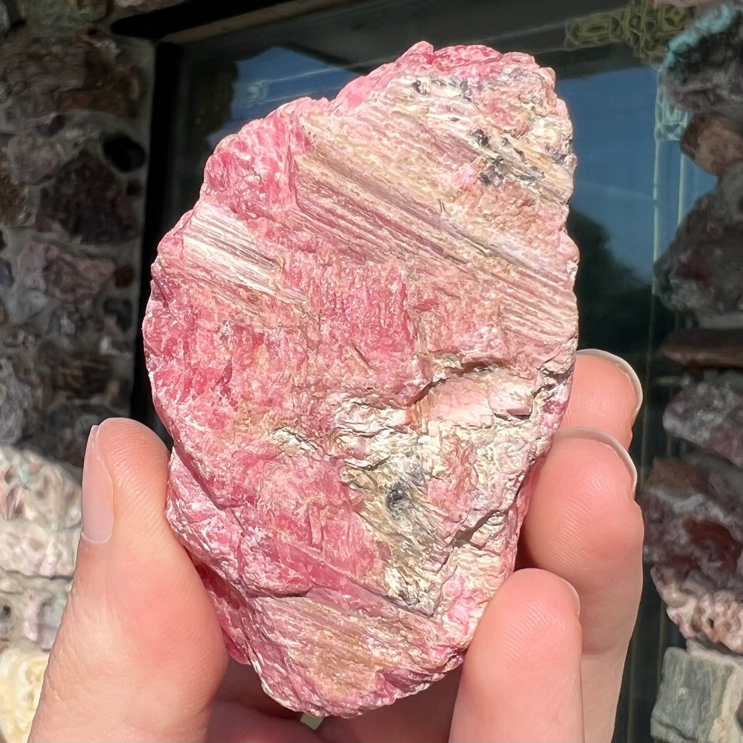 A rough pink rhodonite crystal specimen the size of a small fist.