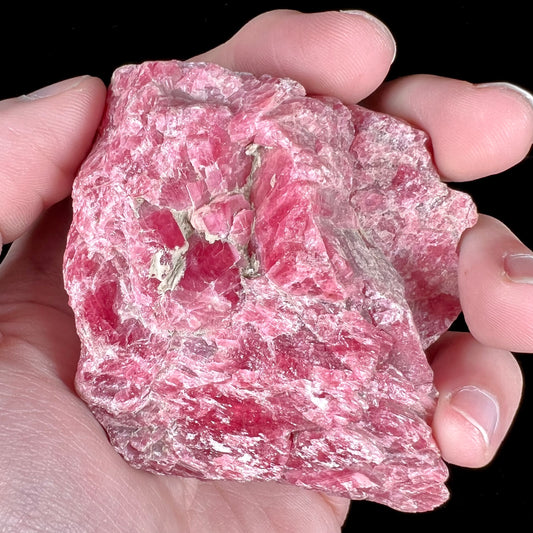 A rough pink rhodonite crystal specimen the size of a small fist.