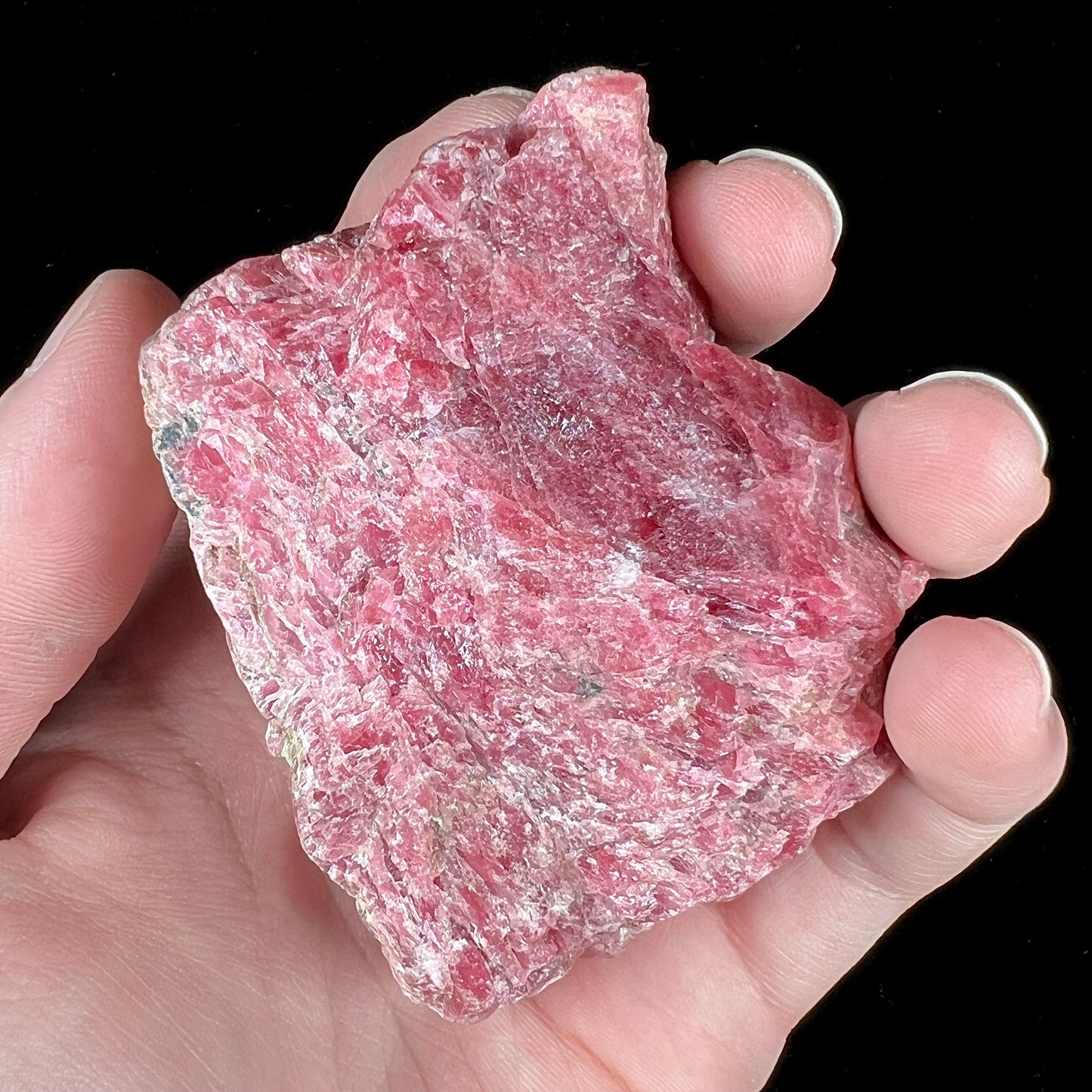 A rough pink rhodonite crystal specimen the size of a small fist.