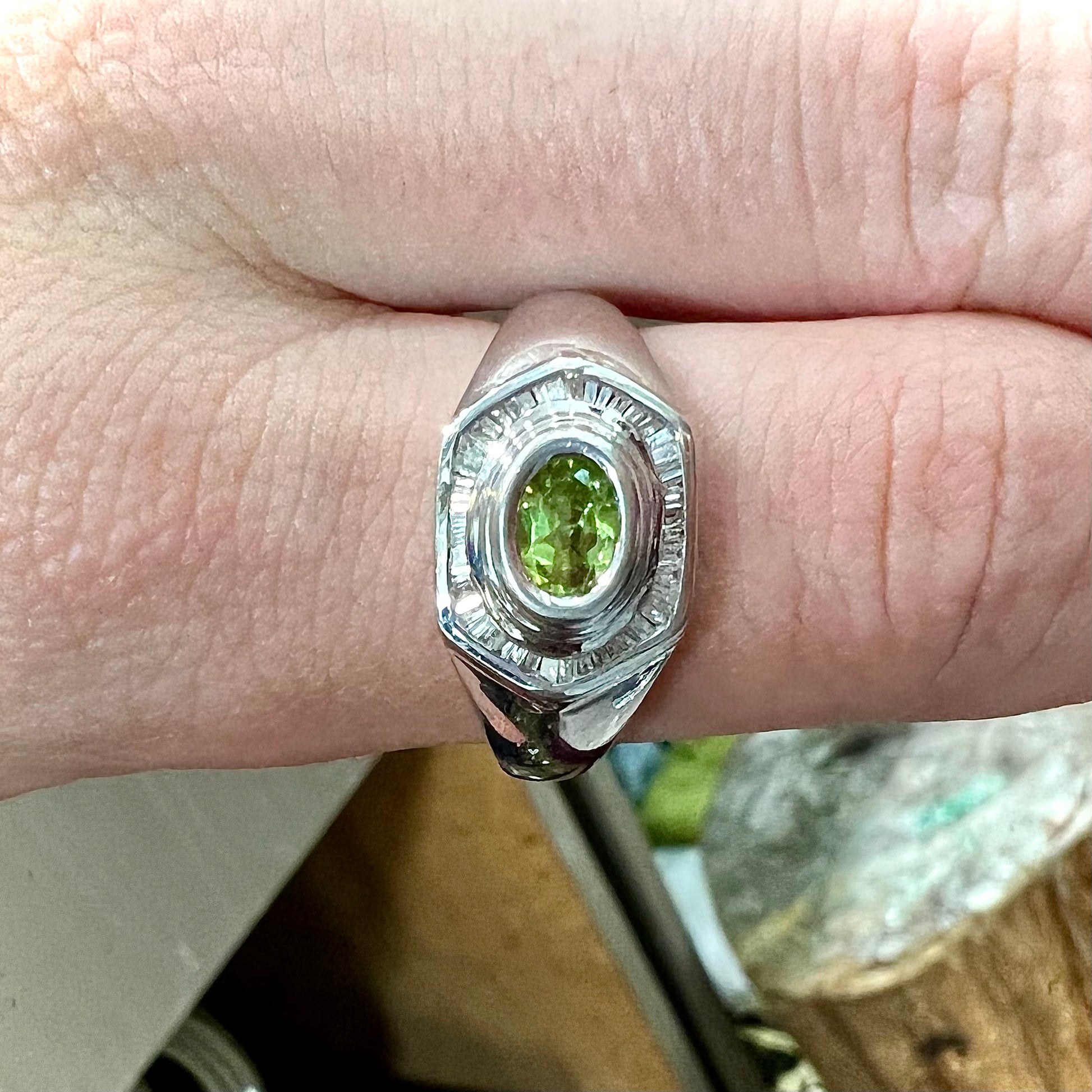 A sterling silver men's ring set with green peridot surrounded by baguette cut diamonds.