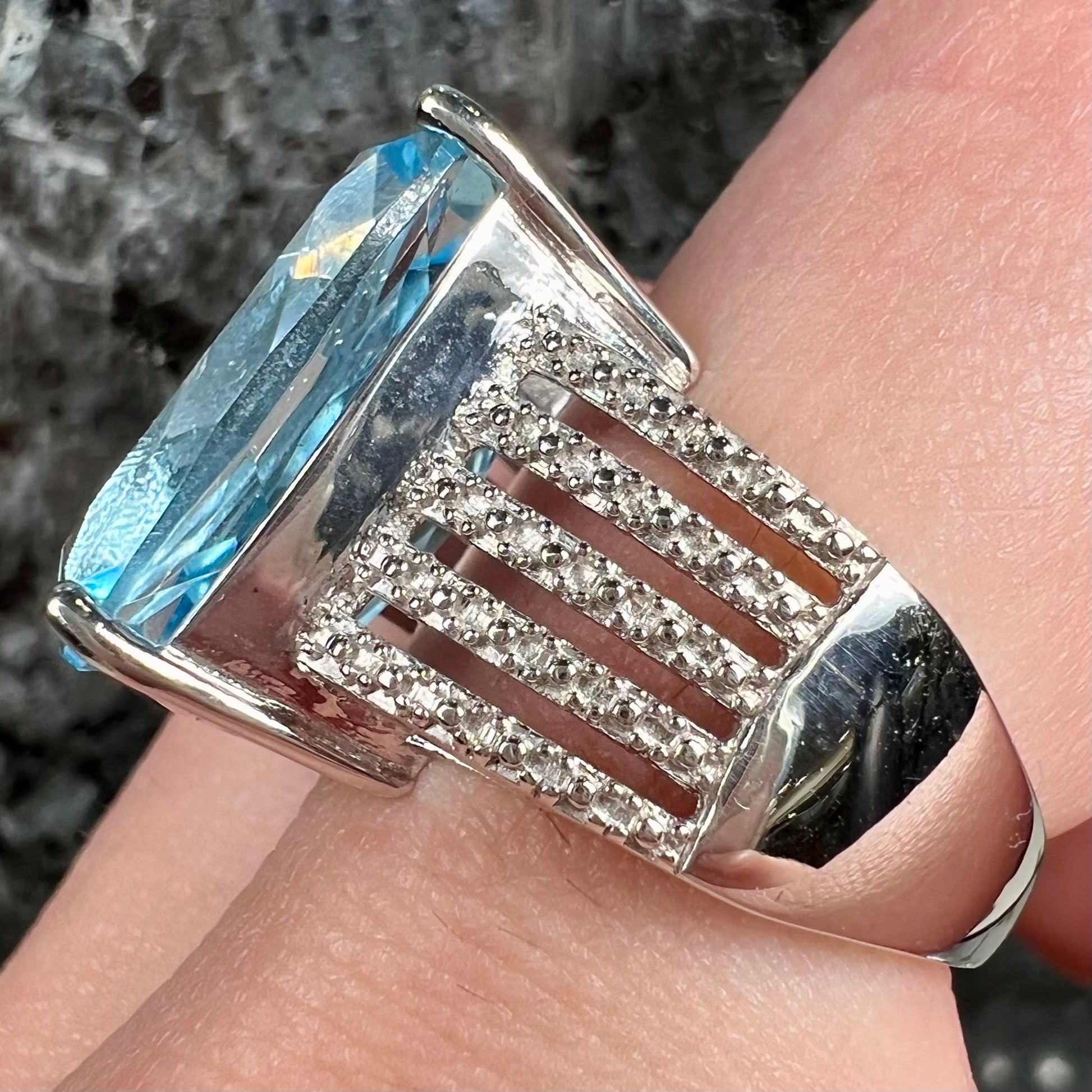 A sterling silver ring prong set with a large, cushion cut sky blue topaz stone.  The shank has been textured to mimic accent stones.