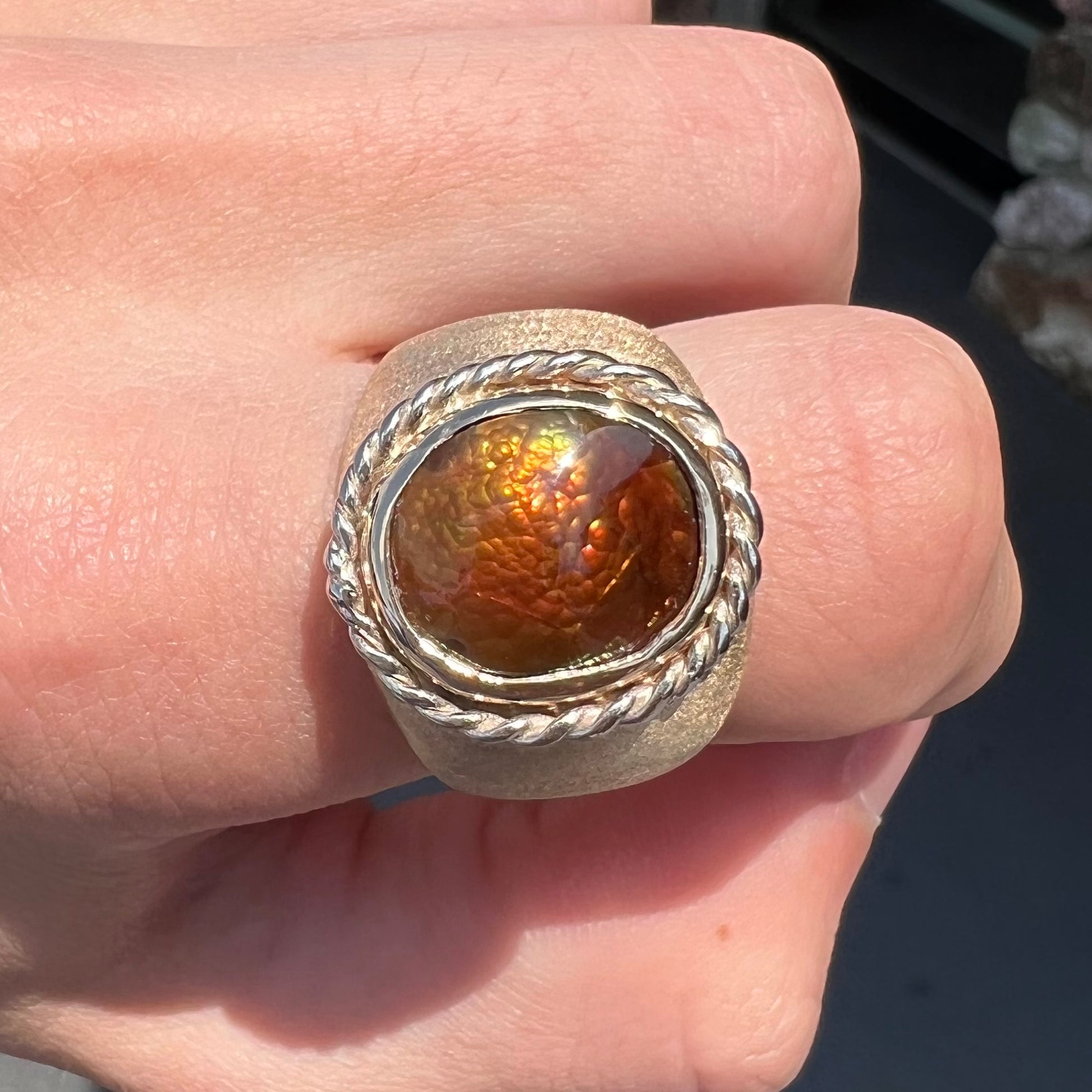 A men's matte finish textured gold fire agate ring.  There is a gold rope bezel around the oval cabochon cut stone.