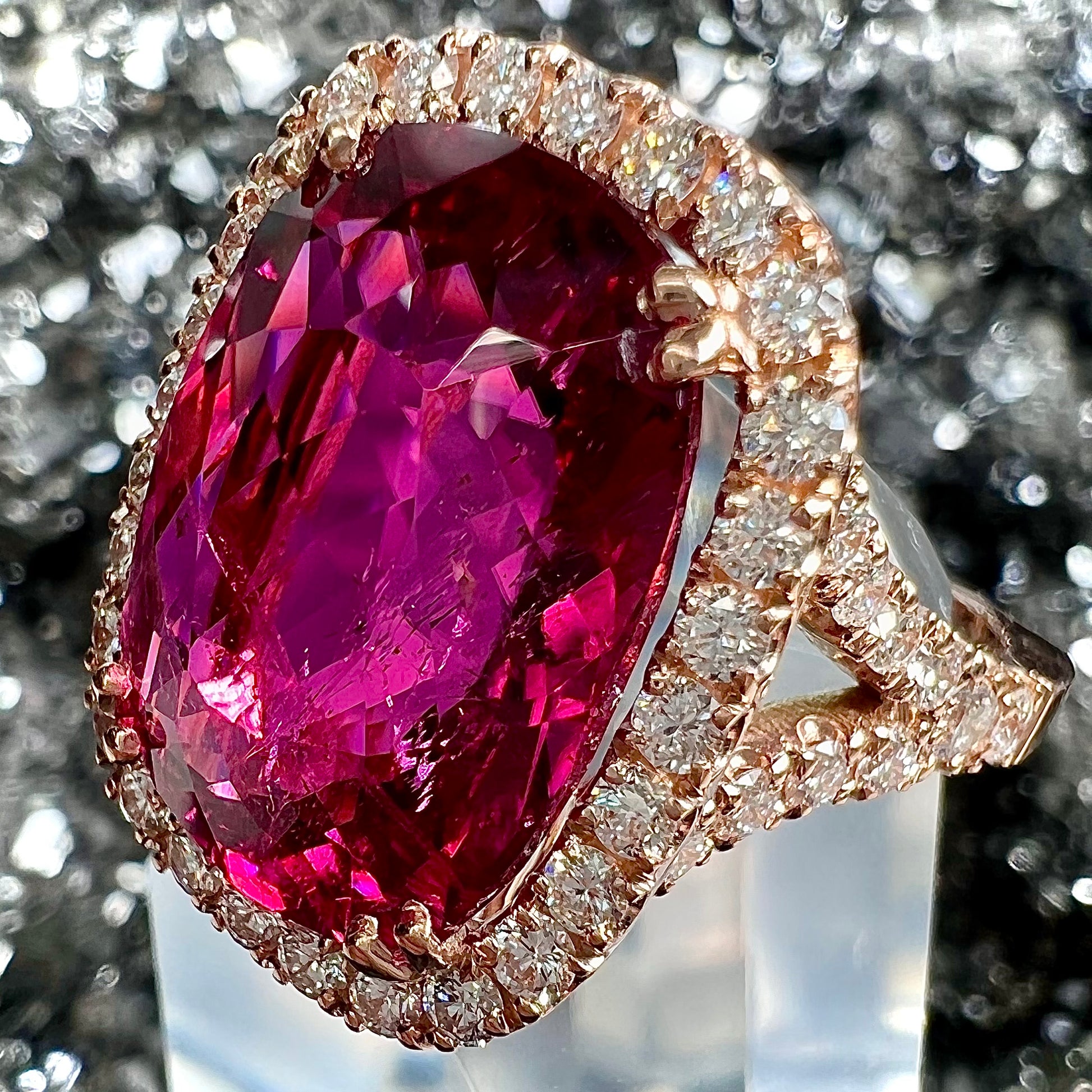 A rose gold, split shank engagement ring set with a cushion cut rubellite tourmaline in a diamond halo.