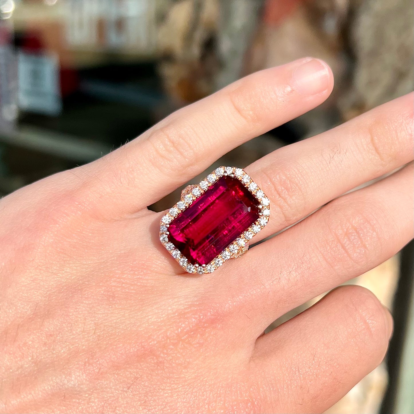 Red emerald cut rubellite tourmaline gemstone set with near flawless round cut diamonds in rose gold.