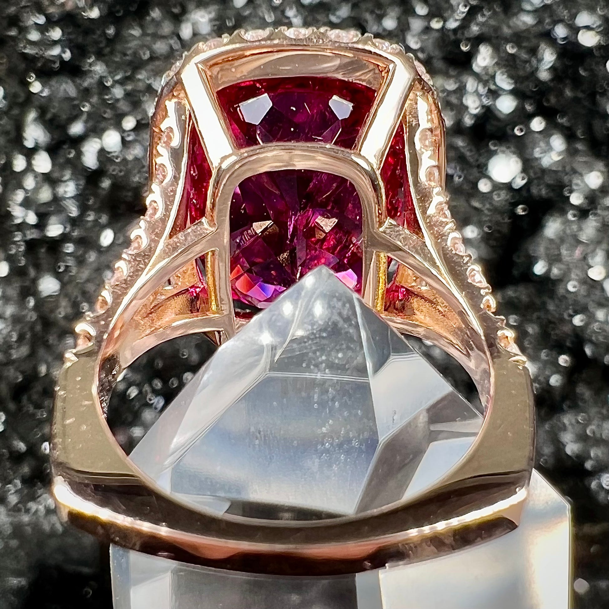 A rose gold, split shank engagement ring set with a cushion cut rubellite tourmaline in a diamond halo.