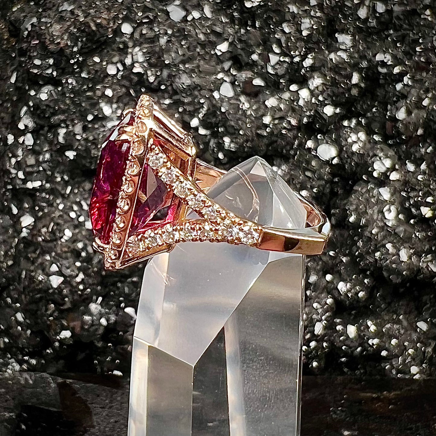 A rose gold, split shank engagement ring set with a cushion cut rubellite tourmaline in a diamond halo.
