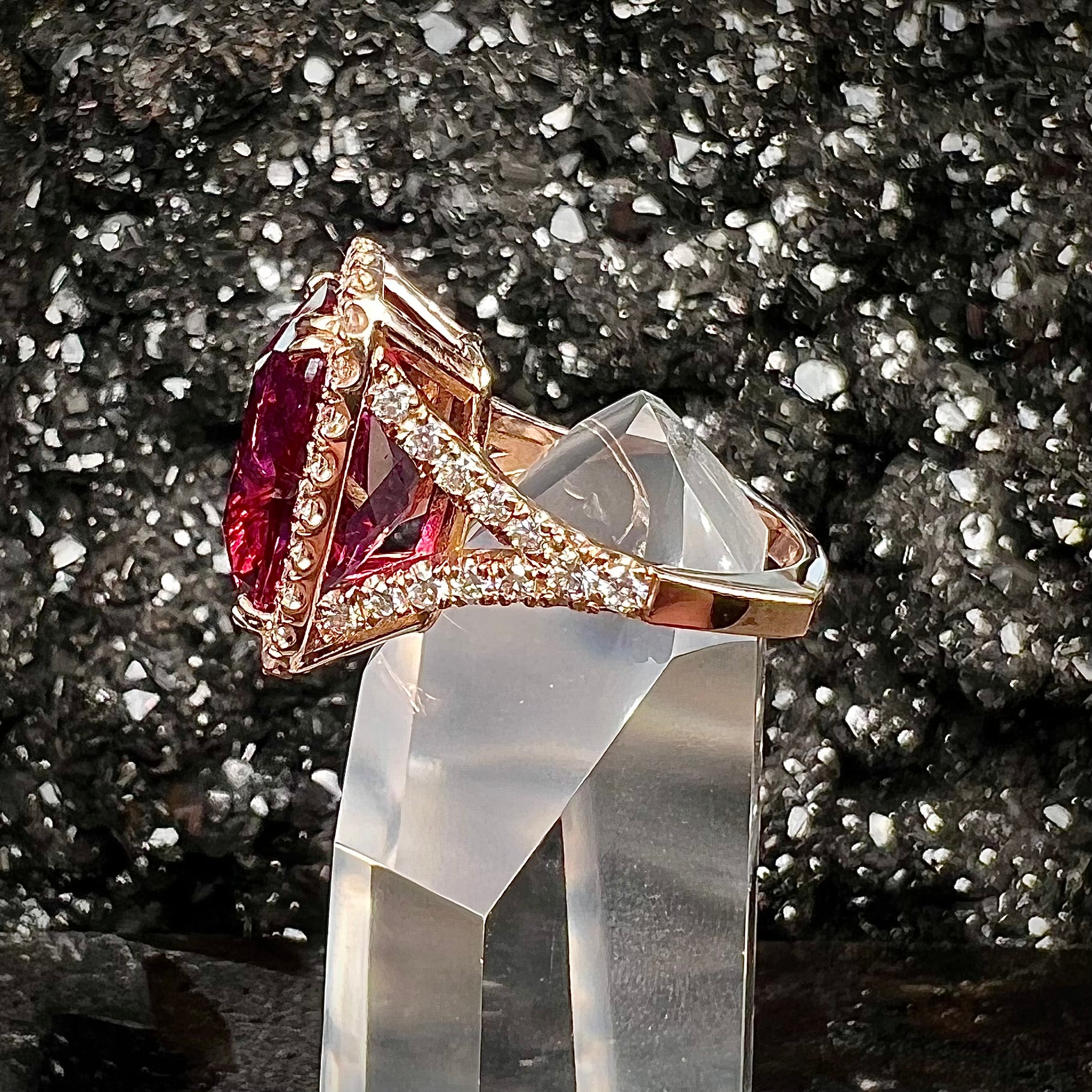 A rose gold, split shank engagement ring set with a cushion cut rubellite tourmaline in a diamond halo.