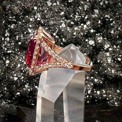 A rose gold, split shank engagement ring set with a cushion cut rubellite tourmaline in a diamond halo.
