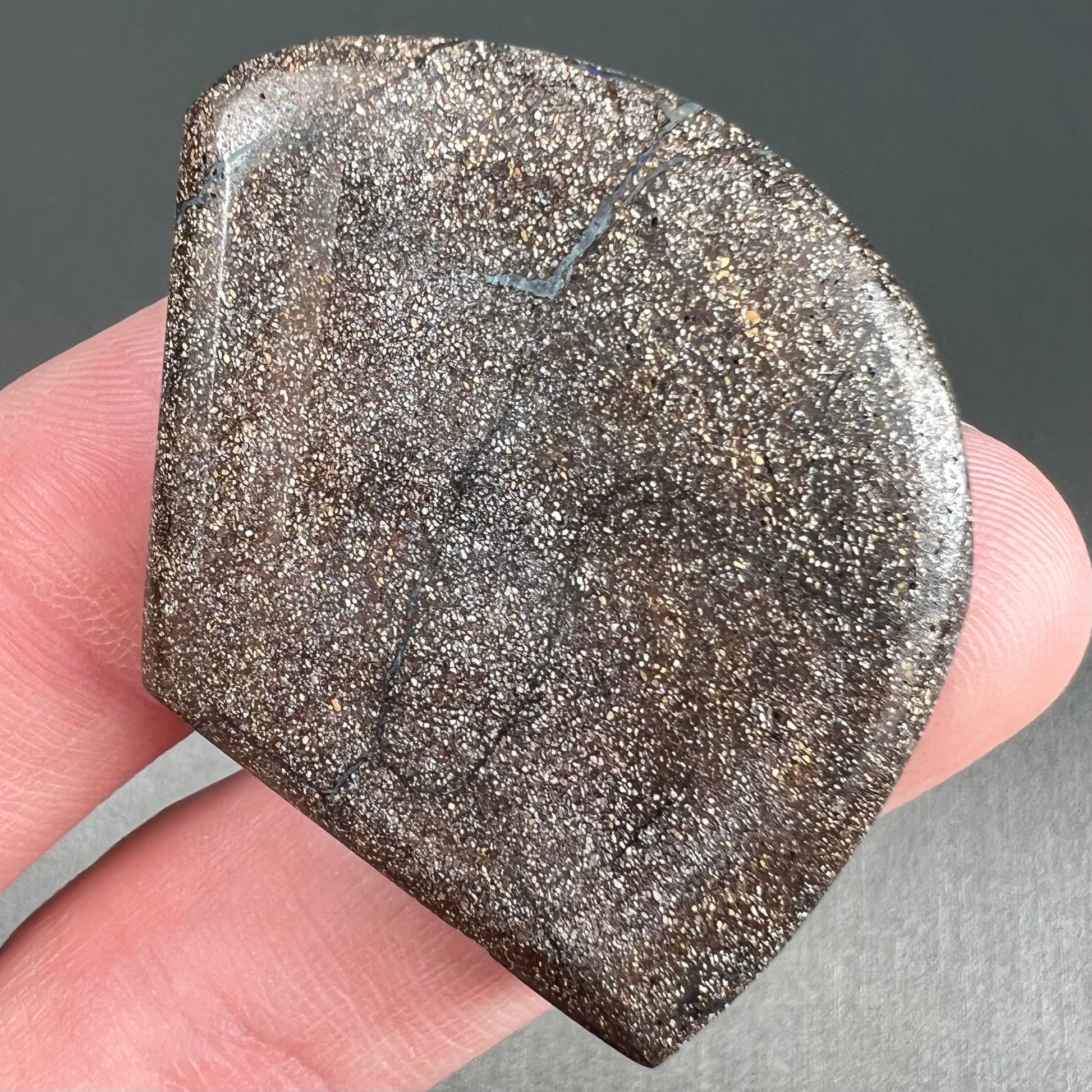 A polished, loose boulder opal stone from Queensland, Australia.  Fire colors are green, blue, purple, and salmon.