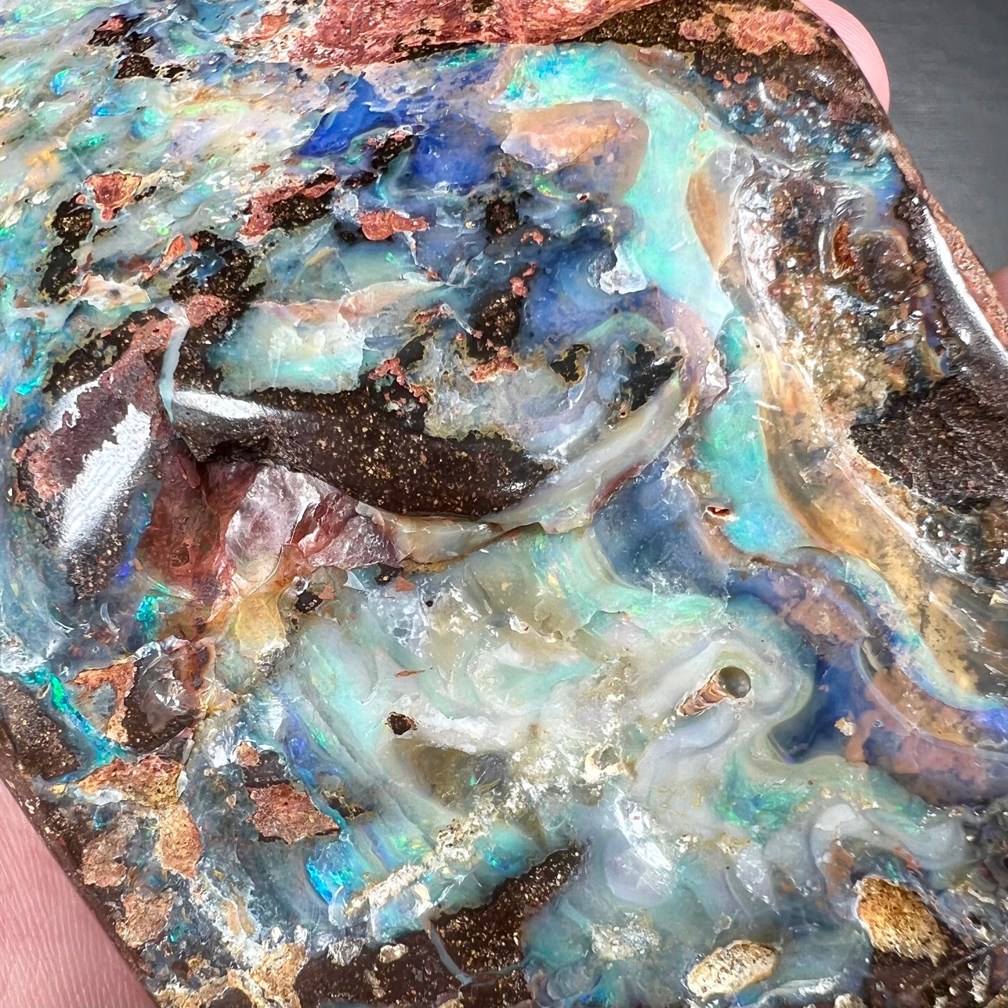 A hand-sized, polished Quilpie boulder opal specimen.  The stone shows blue, green, and orange flashes.
