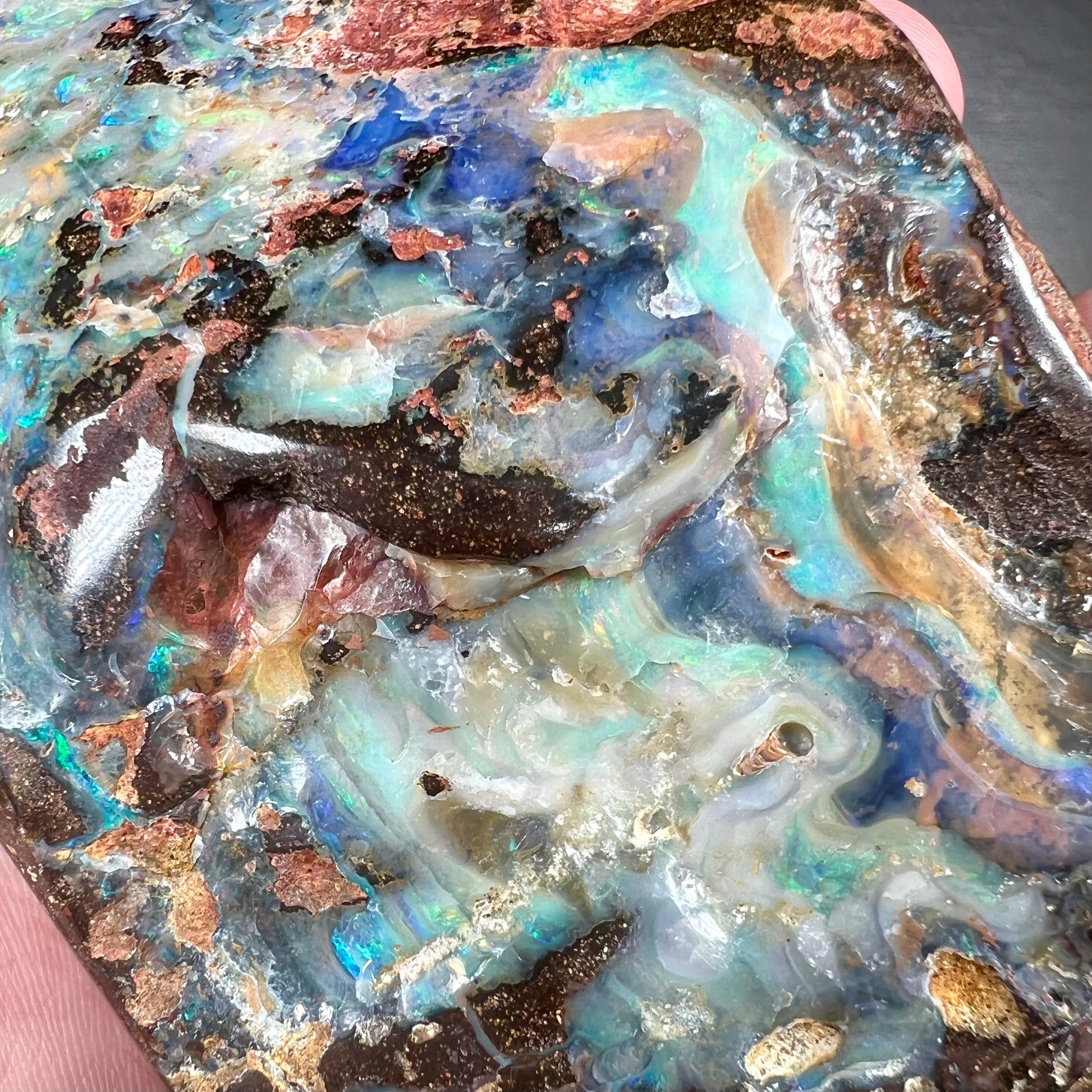 A hand-sized, polished Quilpie boulder opal specimen.  The stone shows blue, green, and orange flashes.