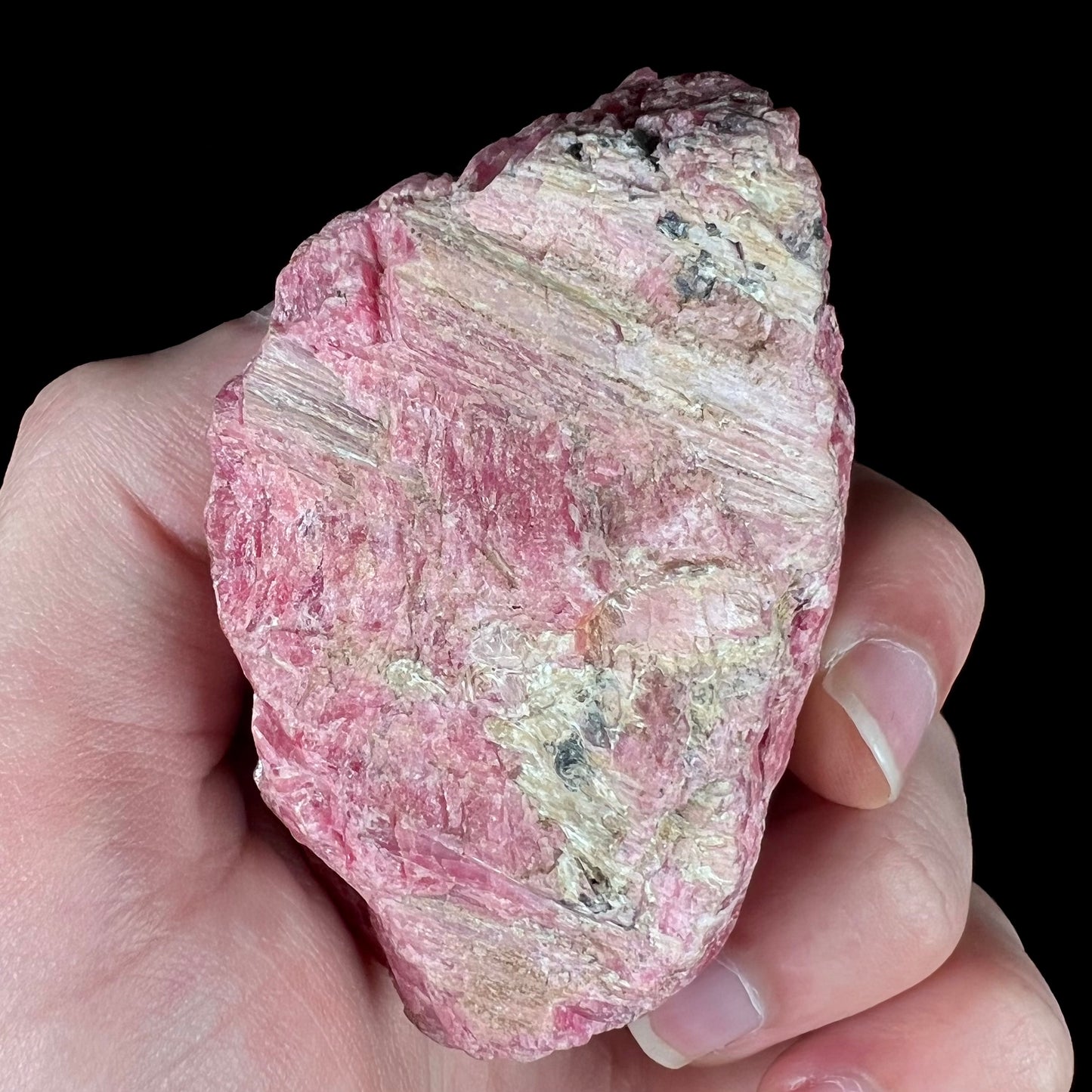 A rough pink rhodonite crystal specimen the size of a small fist.