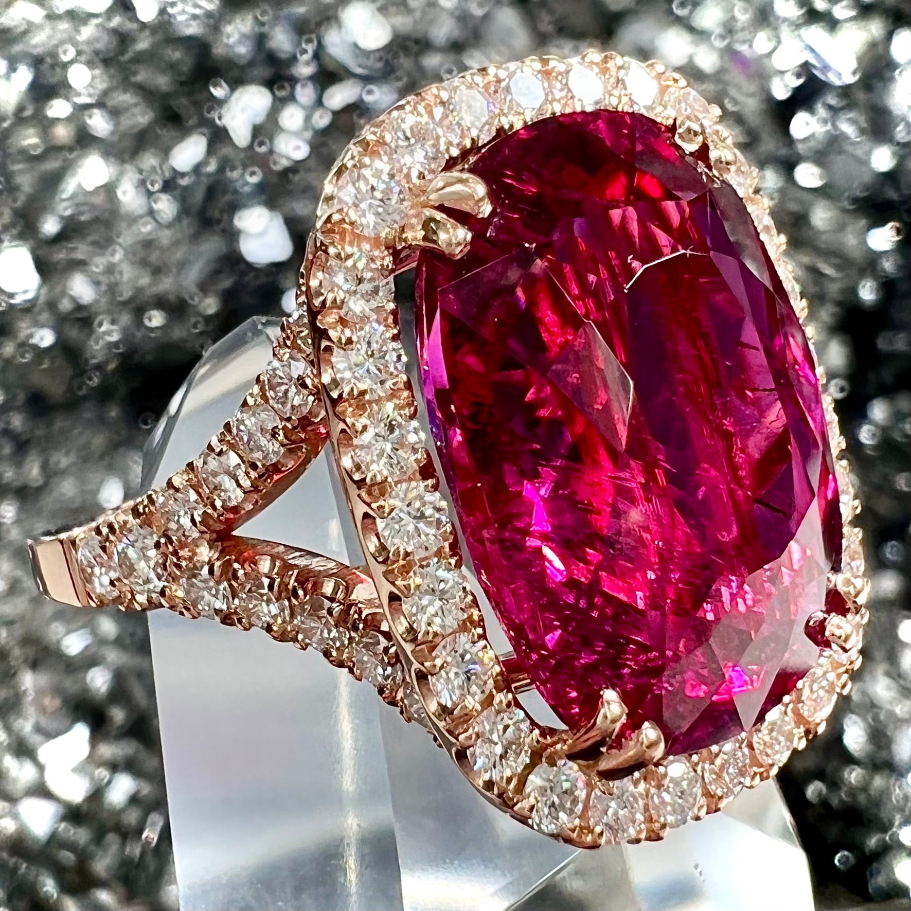A rose gold, split shank engagement ring set with a cushion cut rubellite tourmaline in a diamond halo.