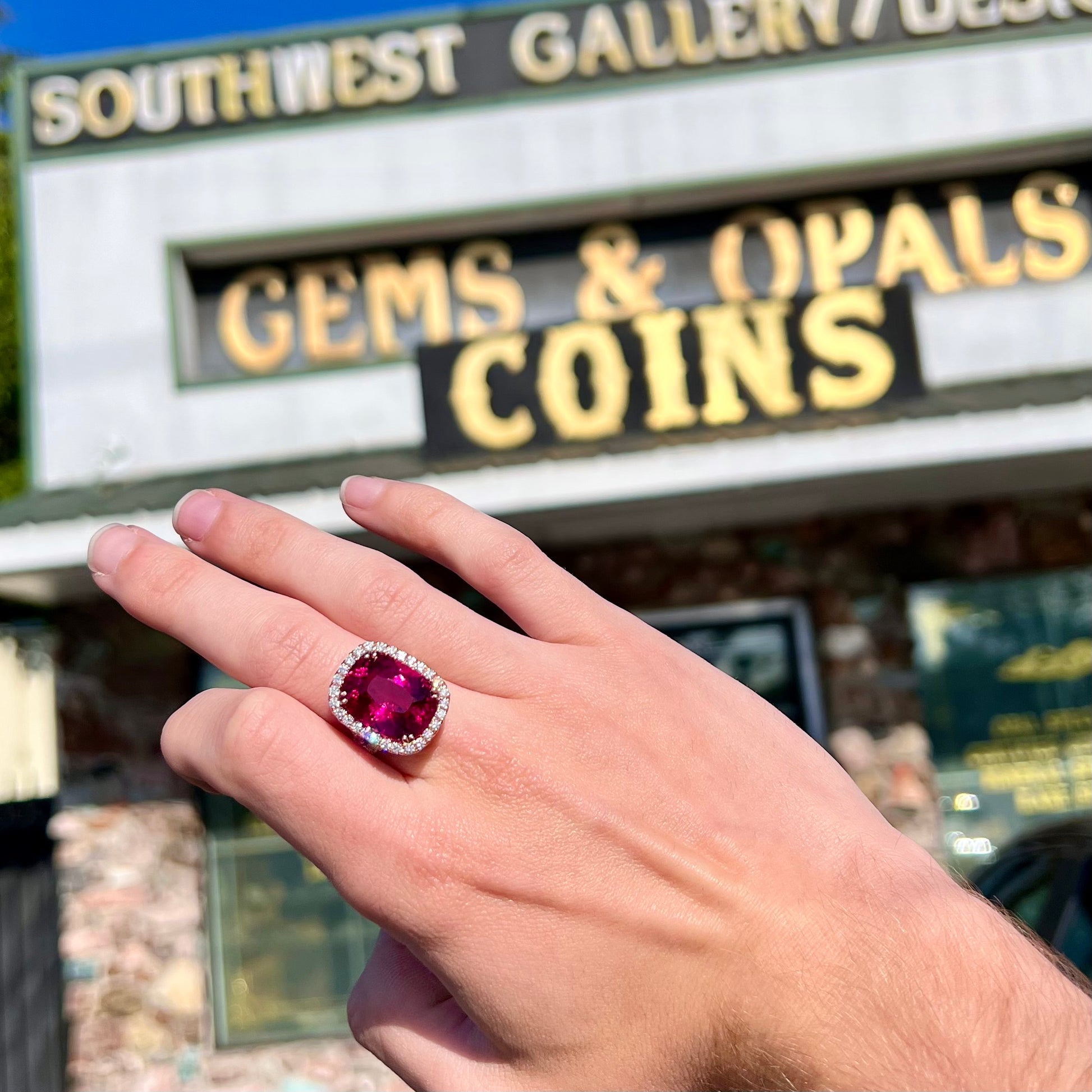 A rose gold, split shank engagement ring set with a cushion cut rubellite tourmaline in a diamond halo.