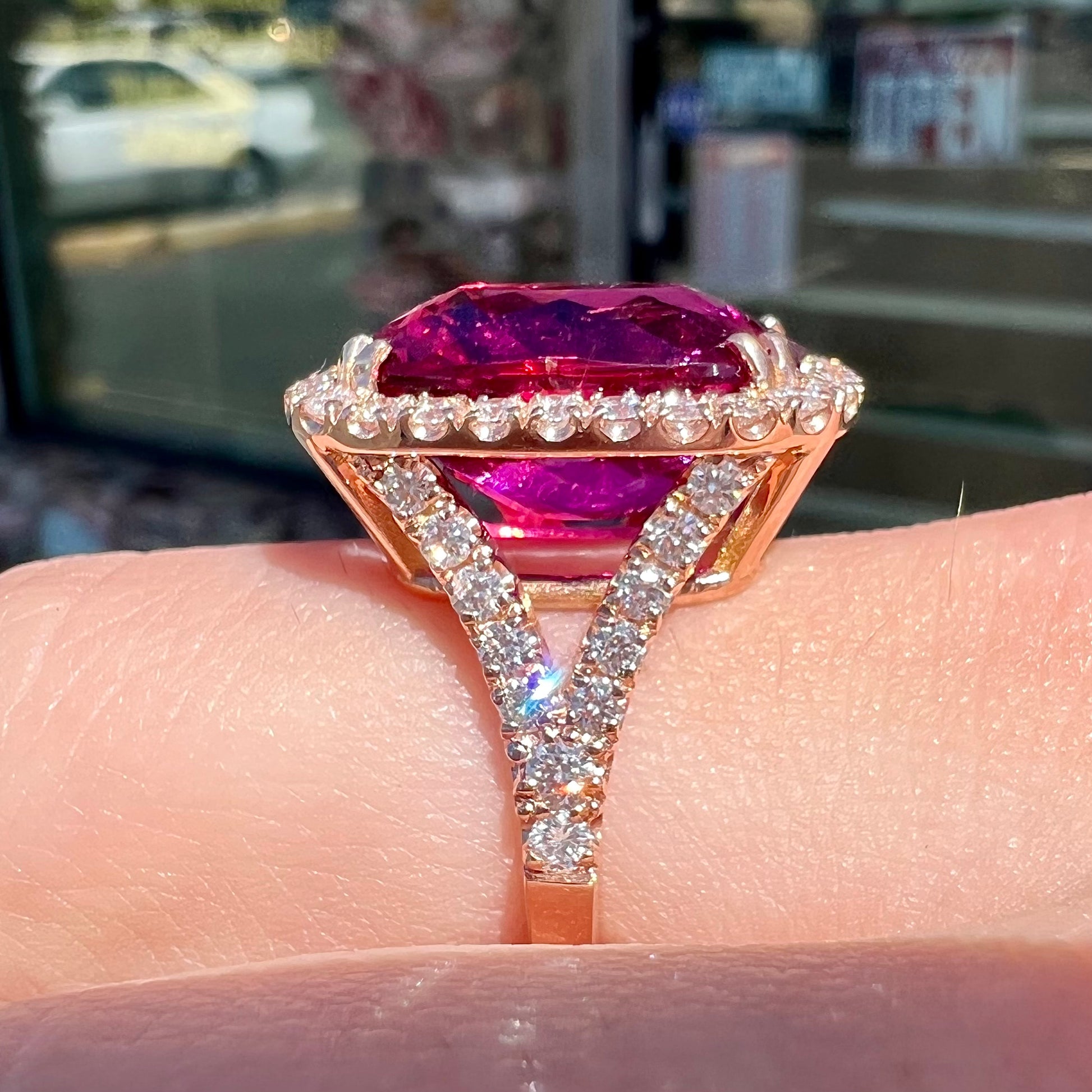 A rose gold, split shank engagement ring set with a cushion cut rubellite tourmaline in a diamond halo.
