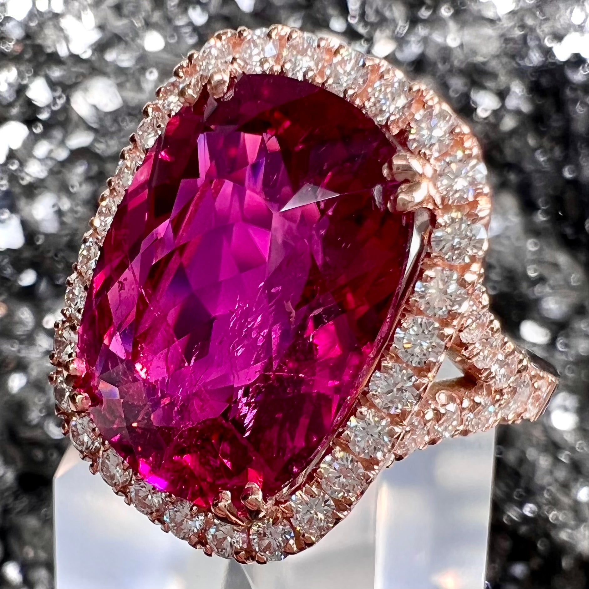 A rose gold, split shank engagement ring set with a cushion cut rubellite tourmaline in a diamond halo.