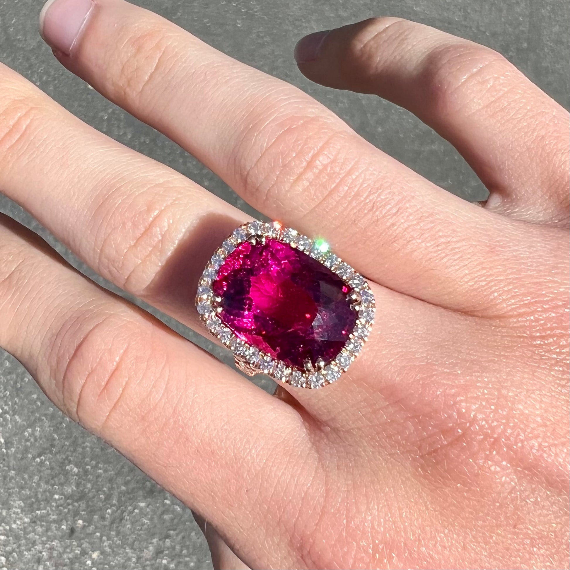 A rose gold, split shank engagement ring set with a cushion cut rubellite tourmaline in a diamond halo.