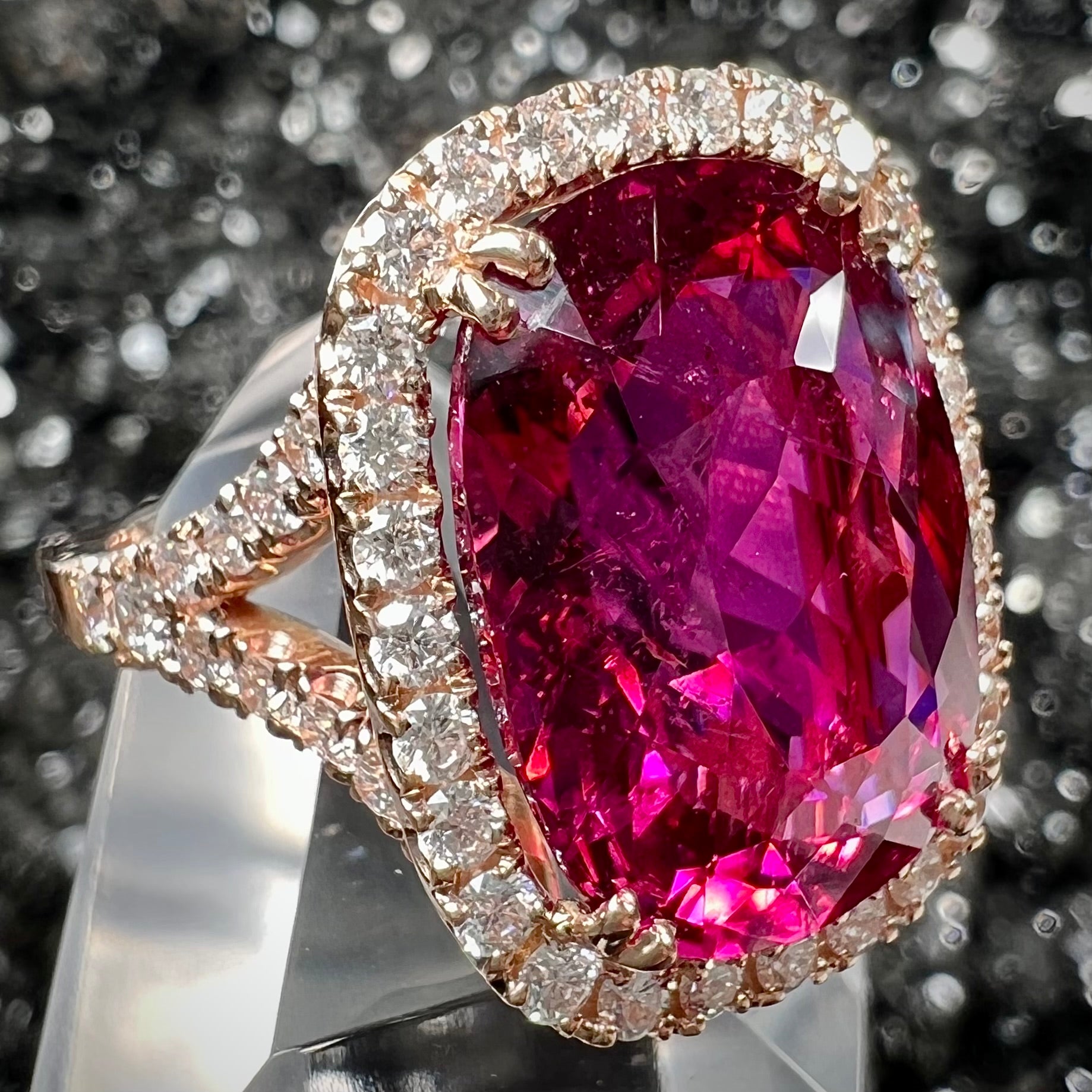 A rose gold, split shank engagement ring set with a cushion cut rubellite tourmaline in a diamond halo.