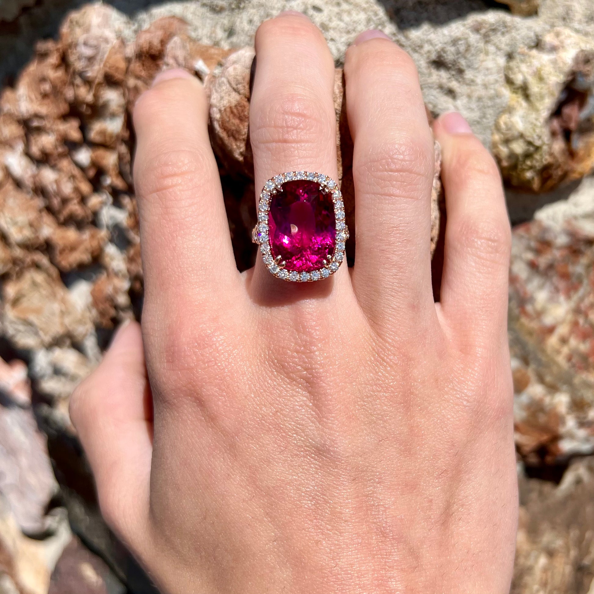 A rose gold, split shank engagement ring set with a cushion cut rubellite tourmaline in a diamond halo.