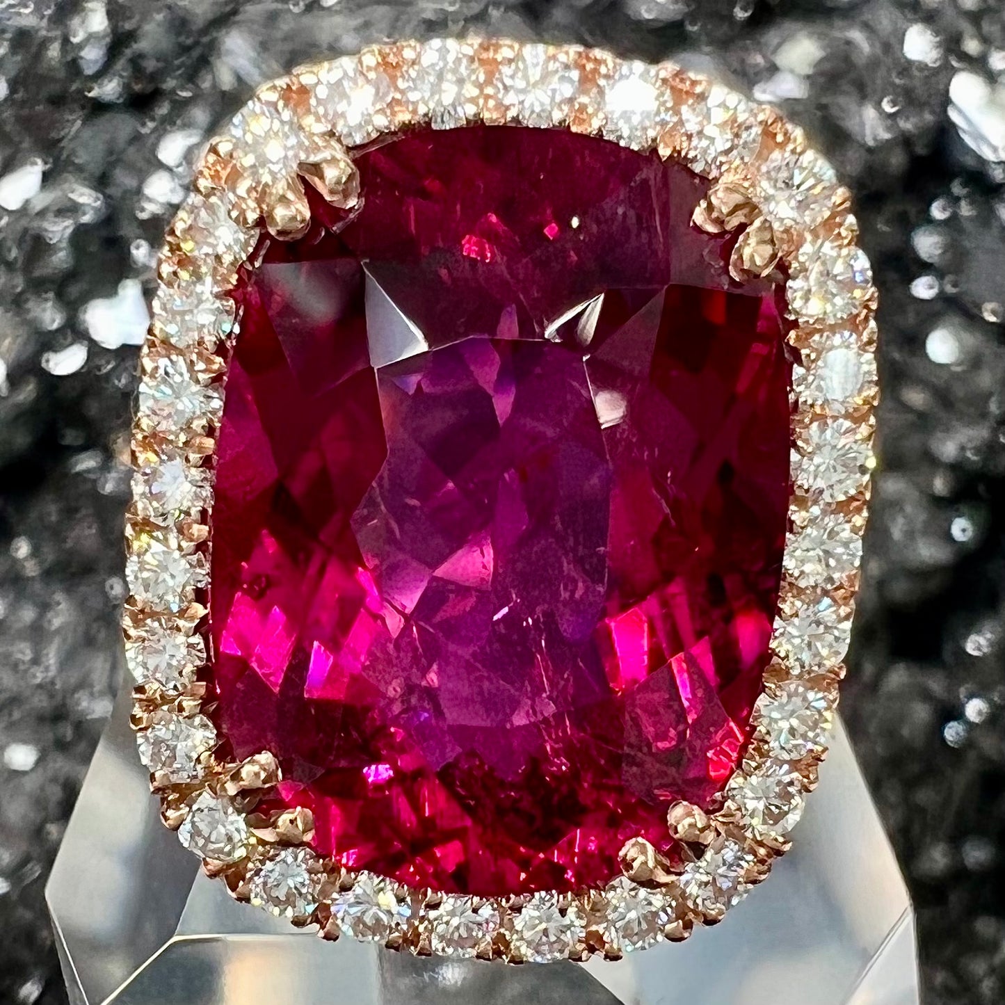A rose gold, split shank engagement ring set with a cushion cut rubellite tourmaline in a diamond halo.