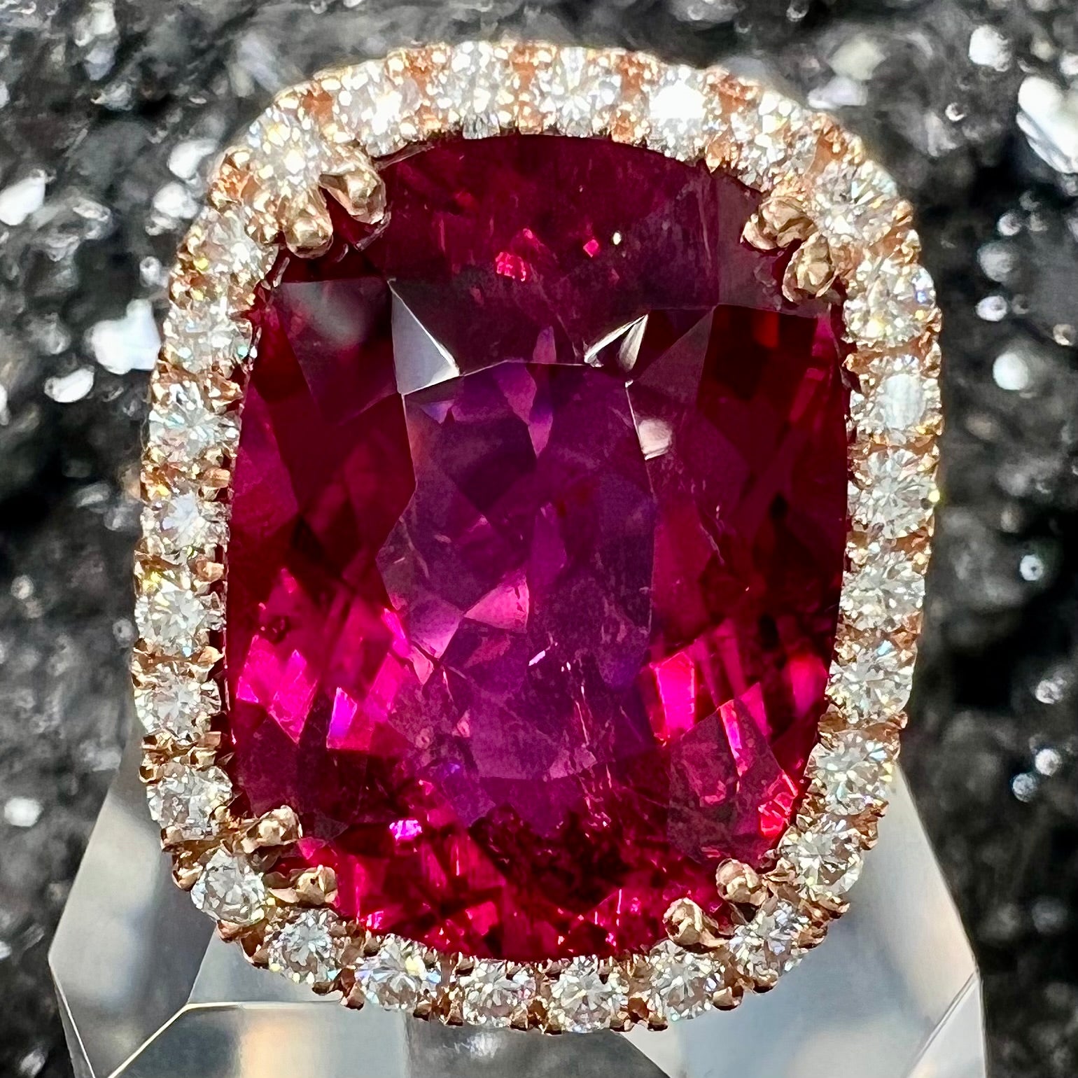 A rose gold, split shank engagement ring set with a cushion cut rubellite tourmaline in a diamond halo.