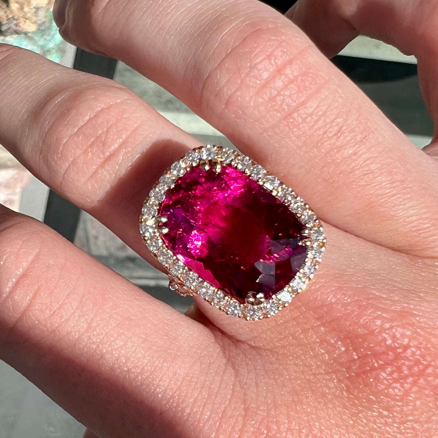 A rose gold, split shank engagement ring set with a cushion cut rubellite tourmaline in a diamond halo.
