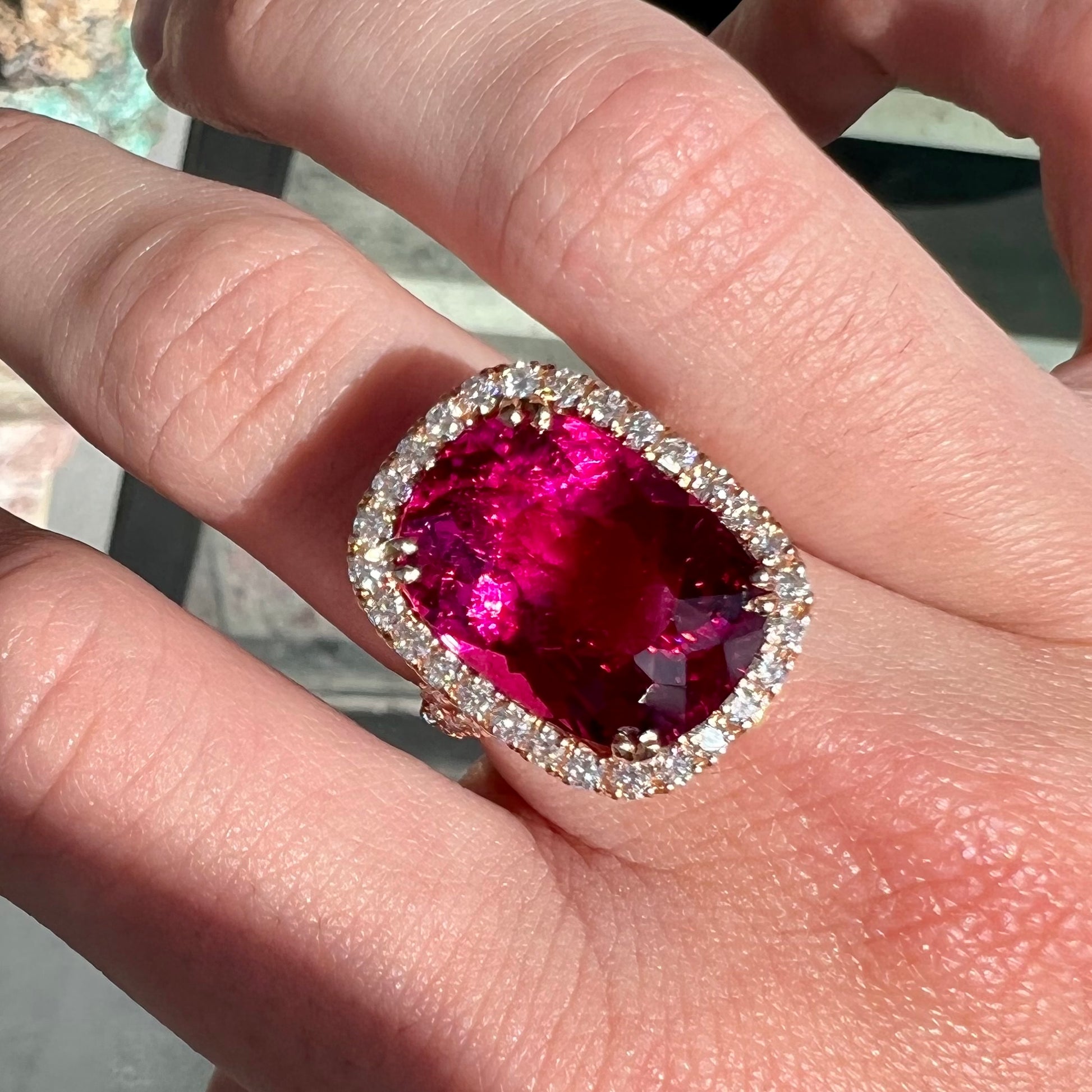 A rose gold, split shank engagement ring set with a cushion cut rubellite tourmaline in a diamond halo.