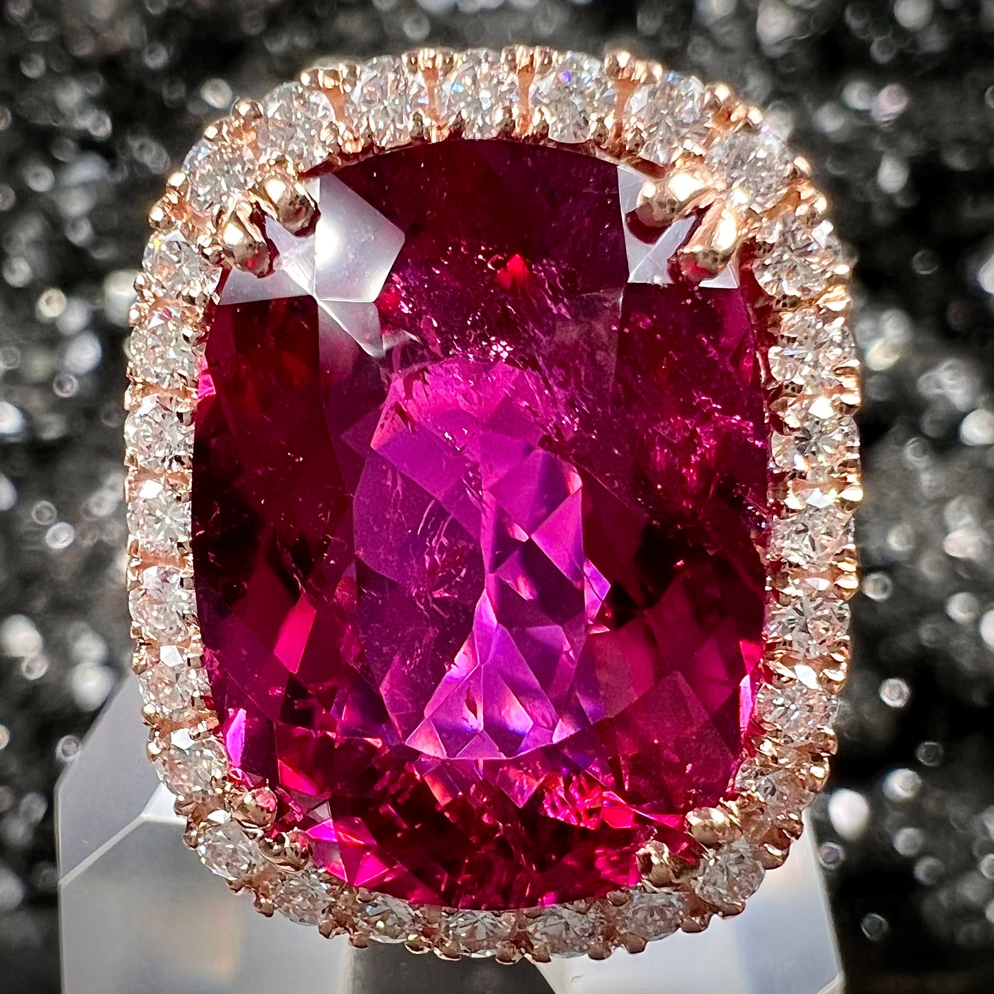 A rose gold, split shank engagement ring set with a cushion cut rubellite tourmaline in a diamond halo.