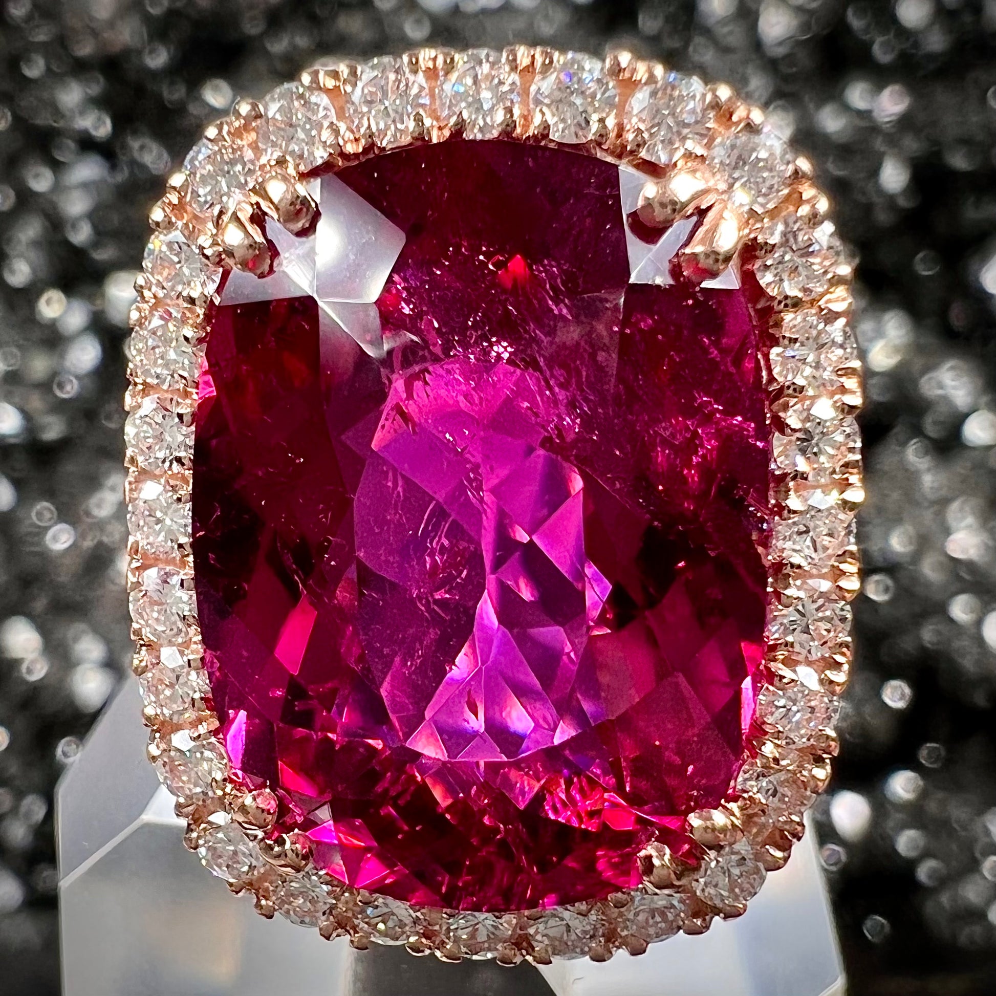 A rose gold, split shank engagement ring set with a cushion cut rubellite tourmaline in a diamond halo.