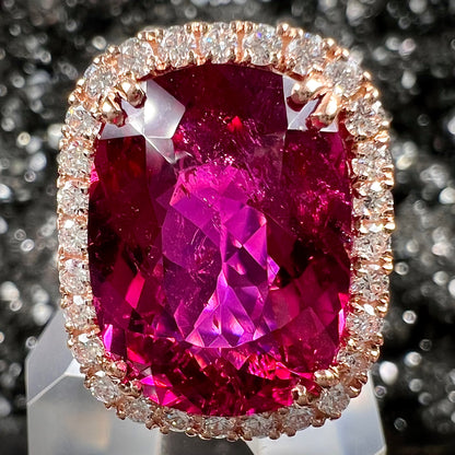 A rose gold, split shank engagement ring set with a cushion cut rubellite tourmaline in a diamond halo.