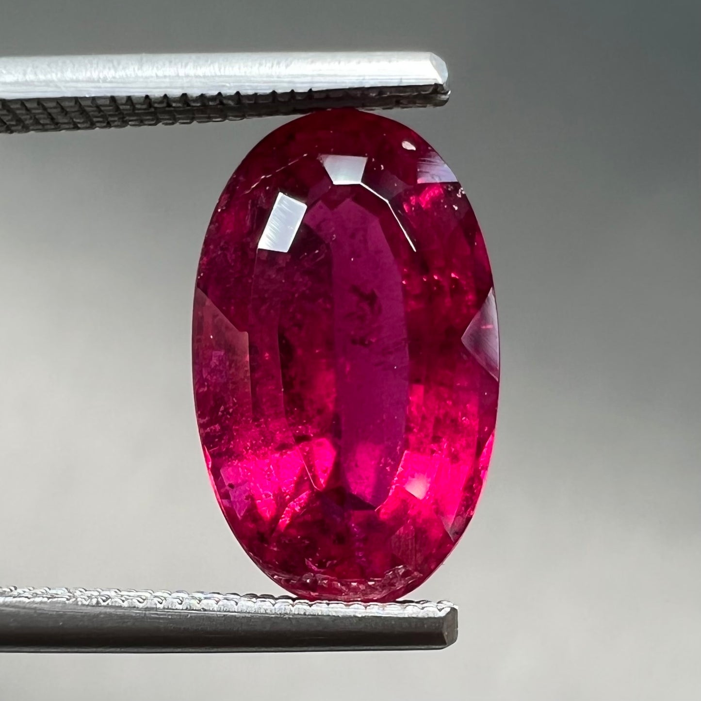 A loose, oval cut, purplish red rubellite tourmaline stone.